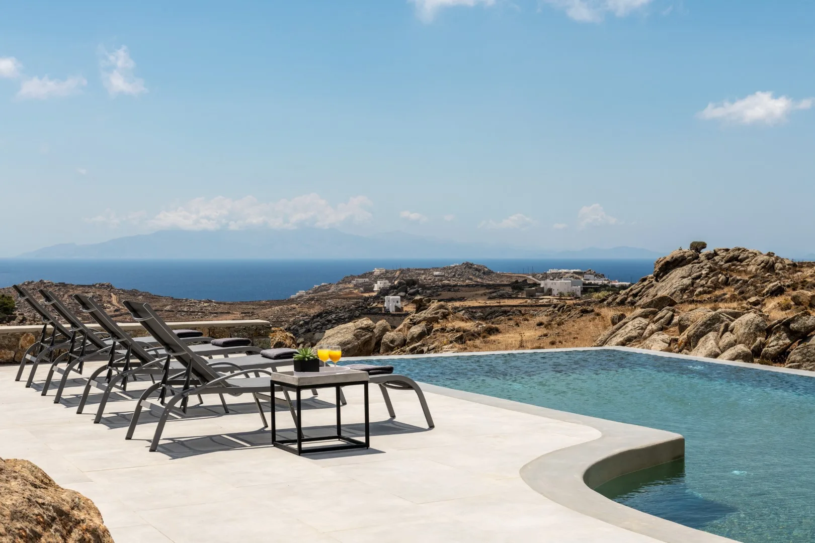 A poolside terrace overlooks the sea, with lounge seating beside the water.