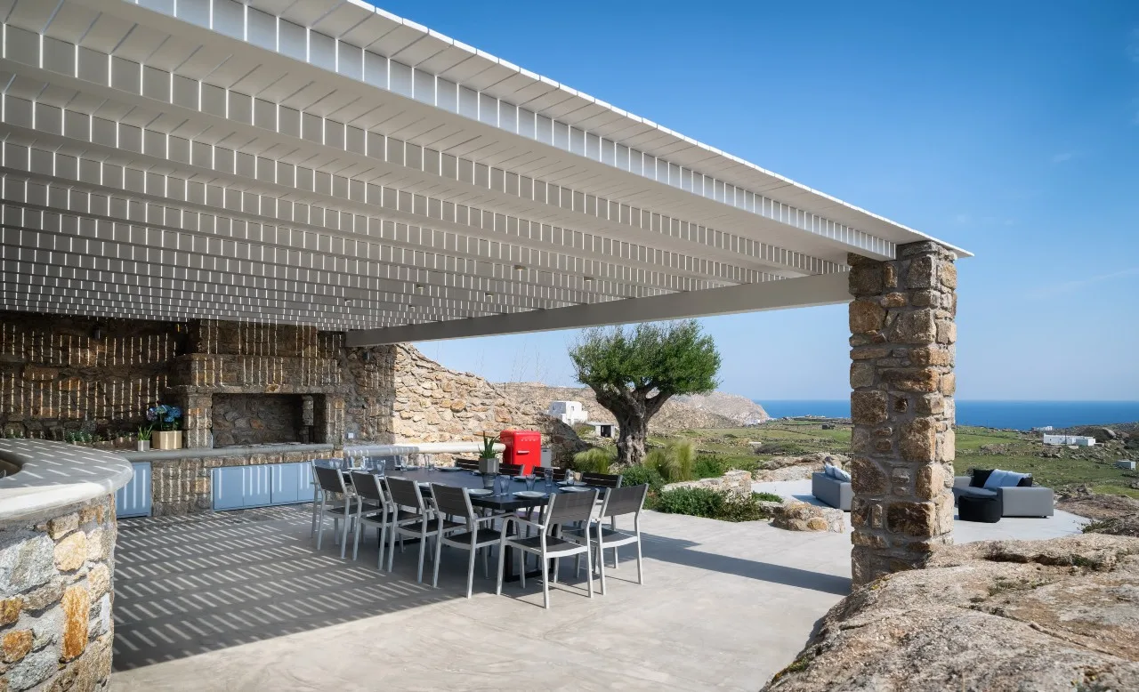 An outdoor dining area sits beneath a broad pergola, overlooking the sea.