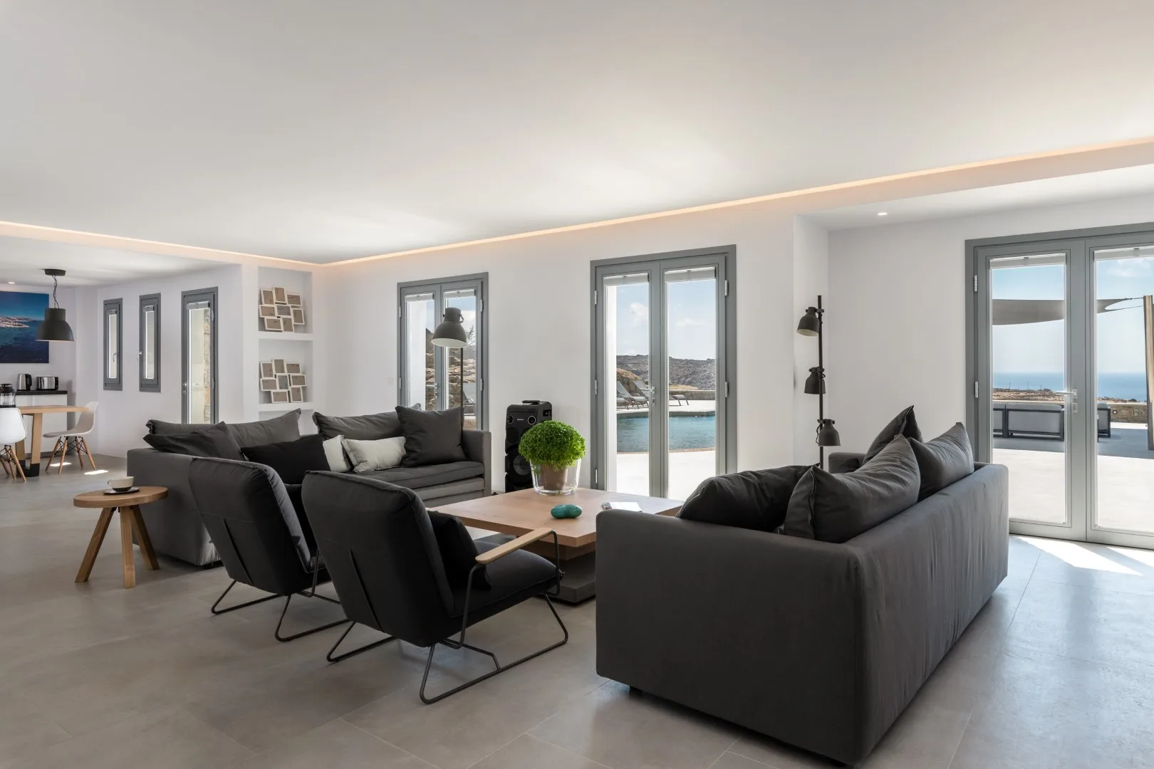 A bright living room with dark seating and glass doors opening onto a sea view.
