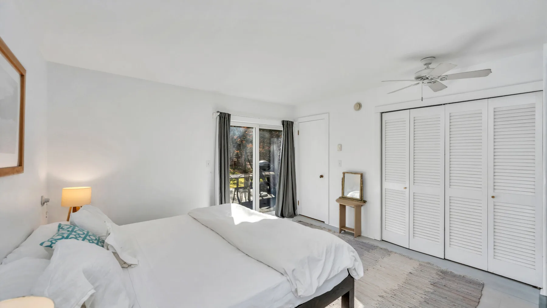 Un dormitorio luminoso con ropa de cama blanca, asientos junto a la cama y un ventilador de techo.
