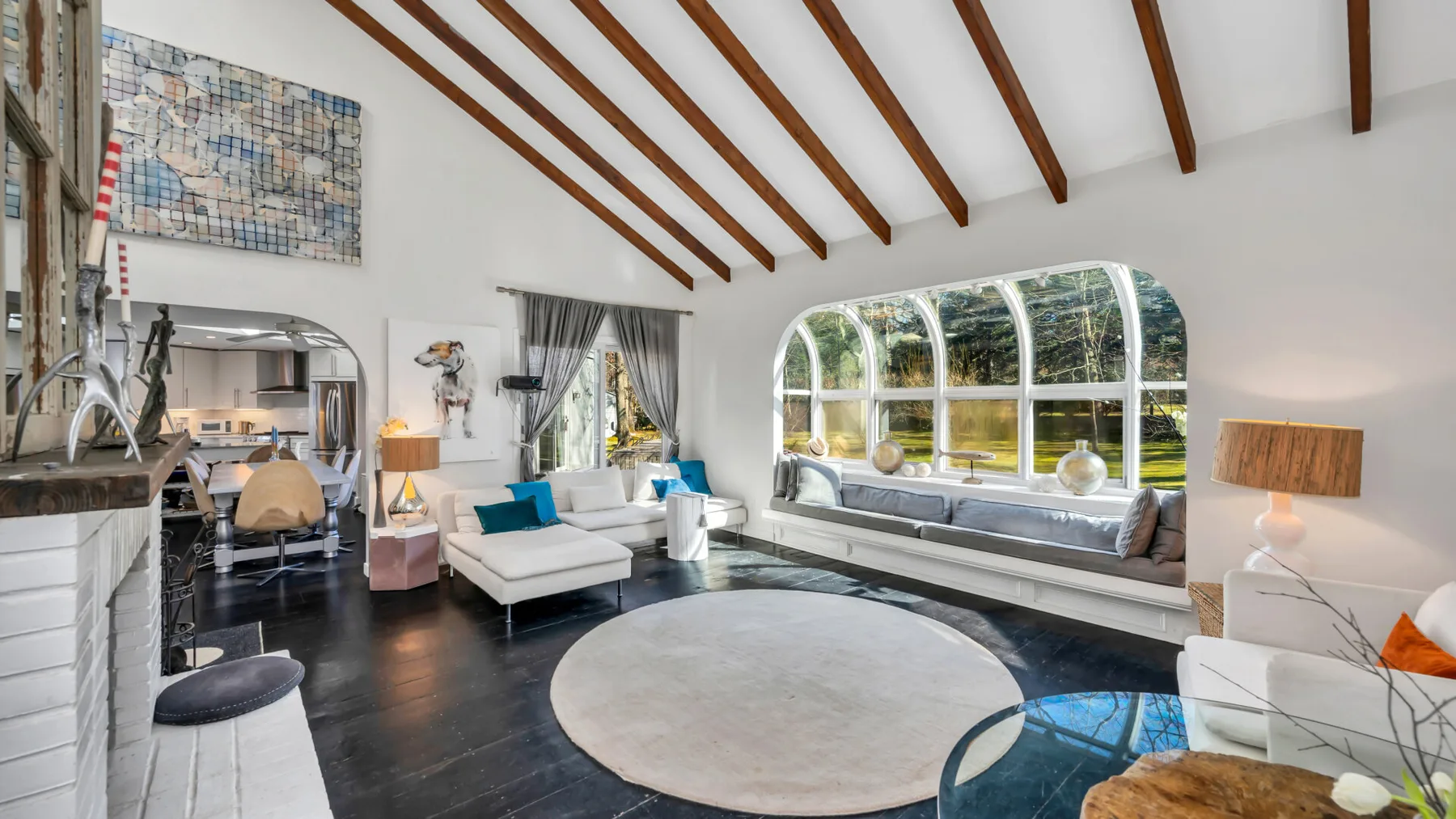 Una sala luminosa con una gran ventana arqueada y vigas de techo expuestas.