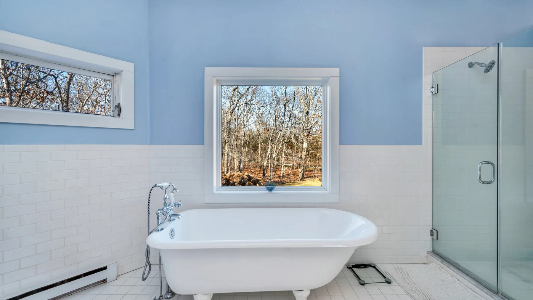 Un baño con una bañera blanca bajo una ventana y una ducha de vidrio.