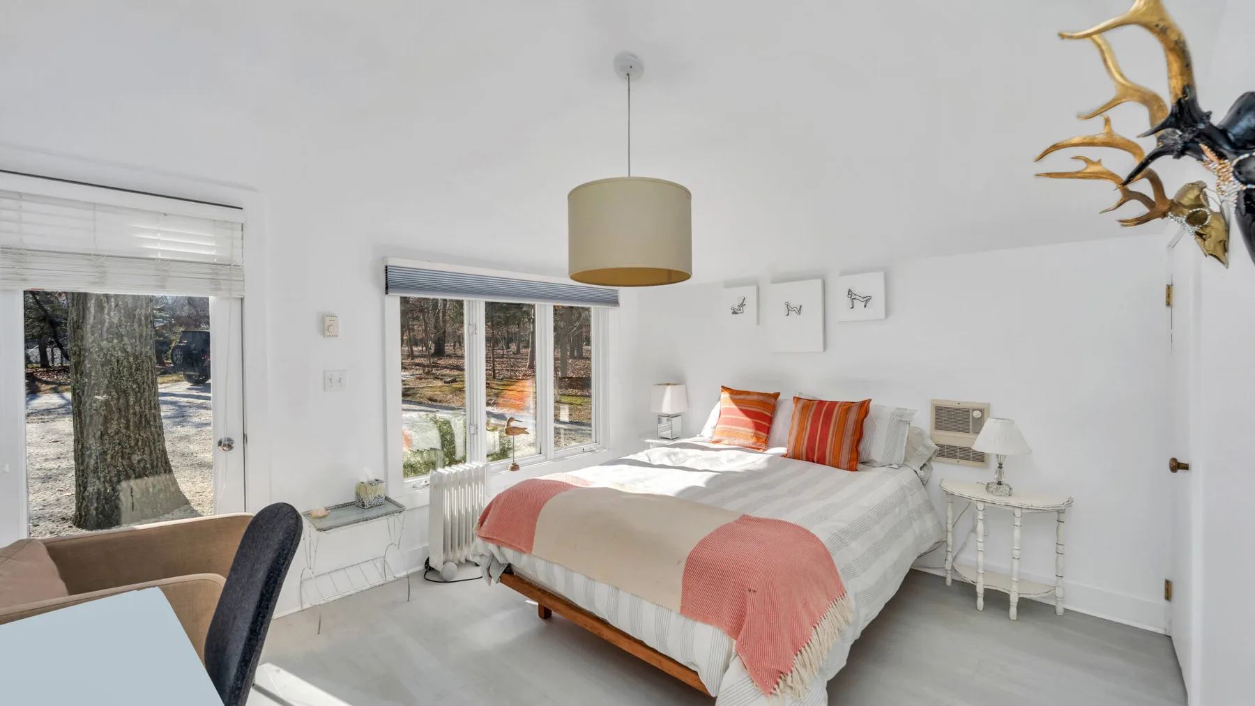 Un dormitorio luminoso con una cama, almohadas a rayas y ventanas.