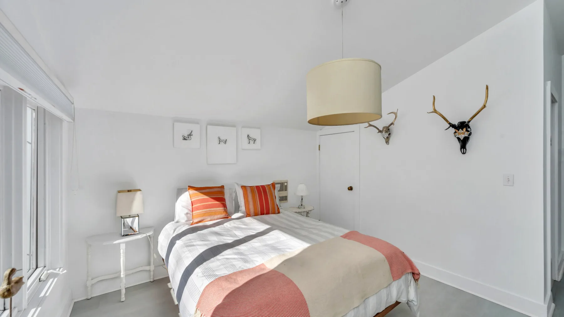 Un dormitorio luminoso cuenta con una cama con almohadas a rayas y cuadros enmarcados.