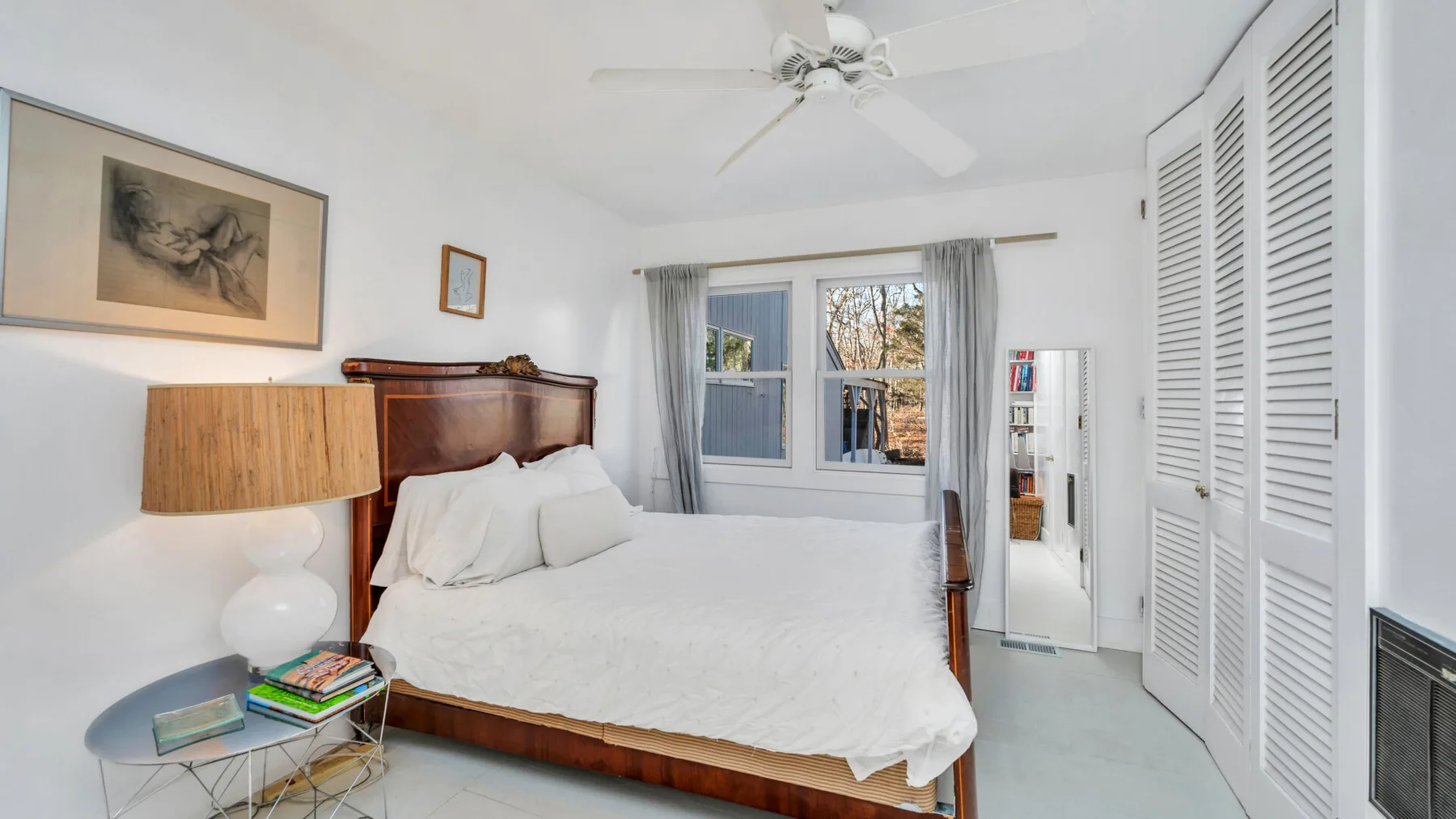 Un dormitorio luminoso con una cama bajo un ventilador de techo y ventanas.