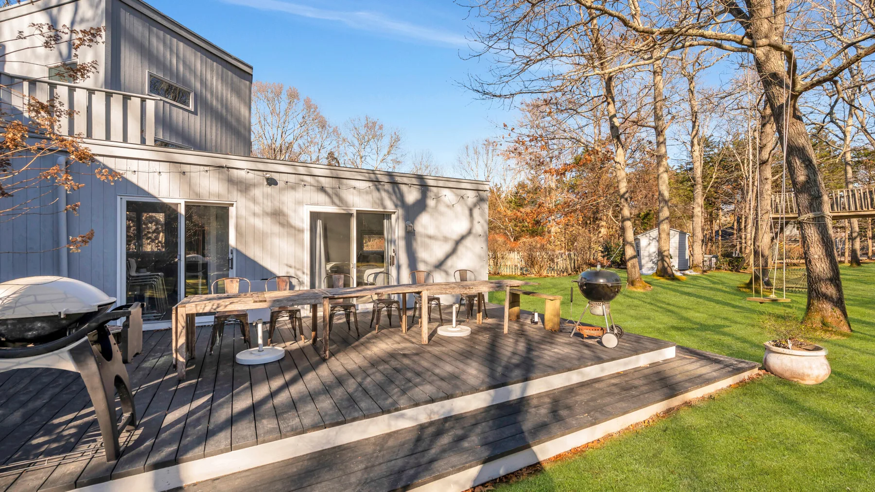 Una casa moderna da a una terraza de madera con asientos al aire libre y una parrilla.