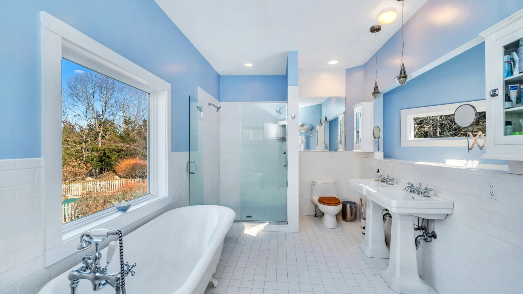 Un baño luminoso con bañera, ducha de vidrio y lavabos con pedestal.