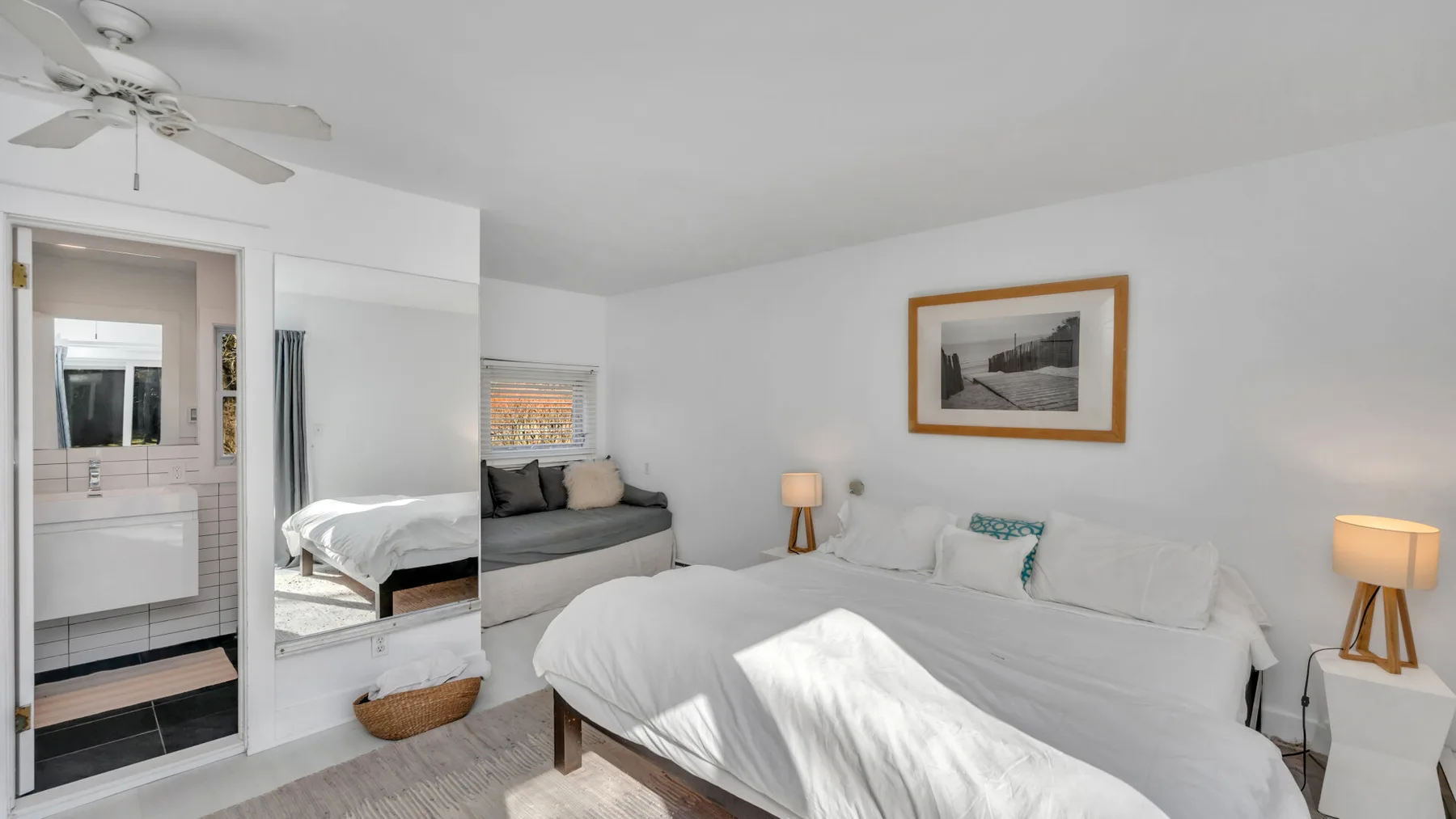 Un dormitorio luminoso con una cama grande y una zona de estar gris.