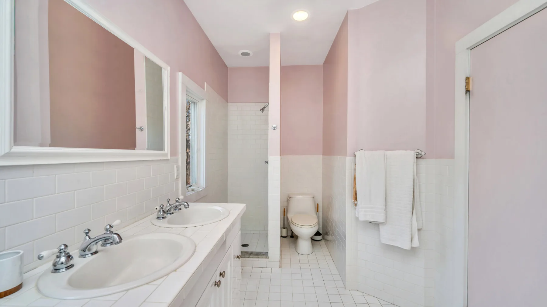 Un baño rosa con lavabo doble y ducha.