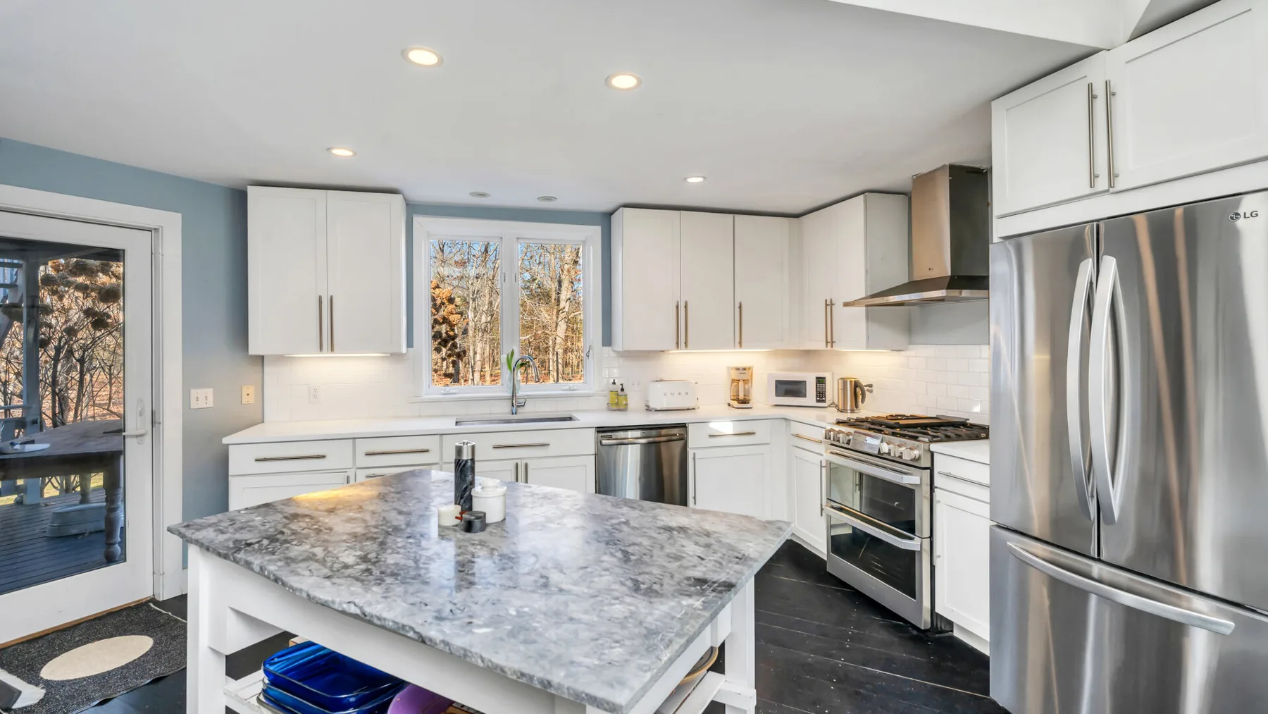 Una cocina luminosa cuenta con gabinetes blancos, una isla grande y electrodomésticos de acero inoxidable.