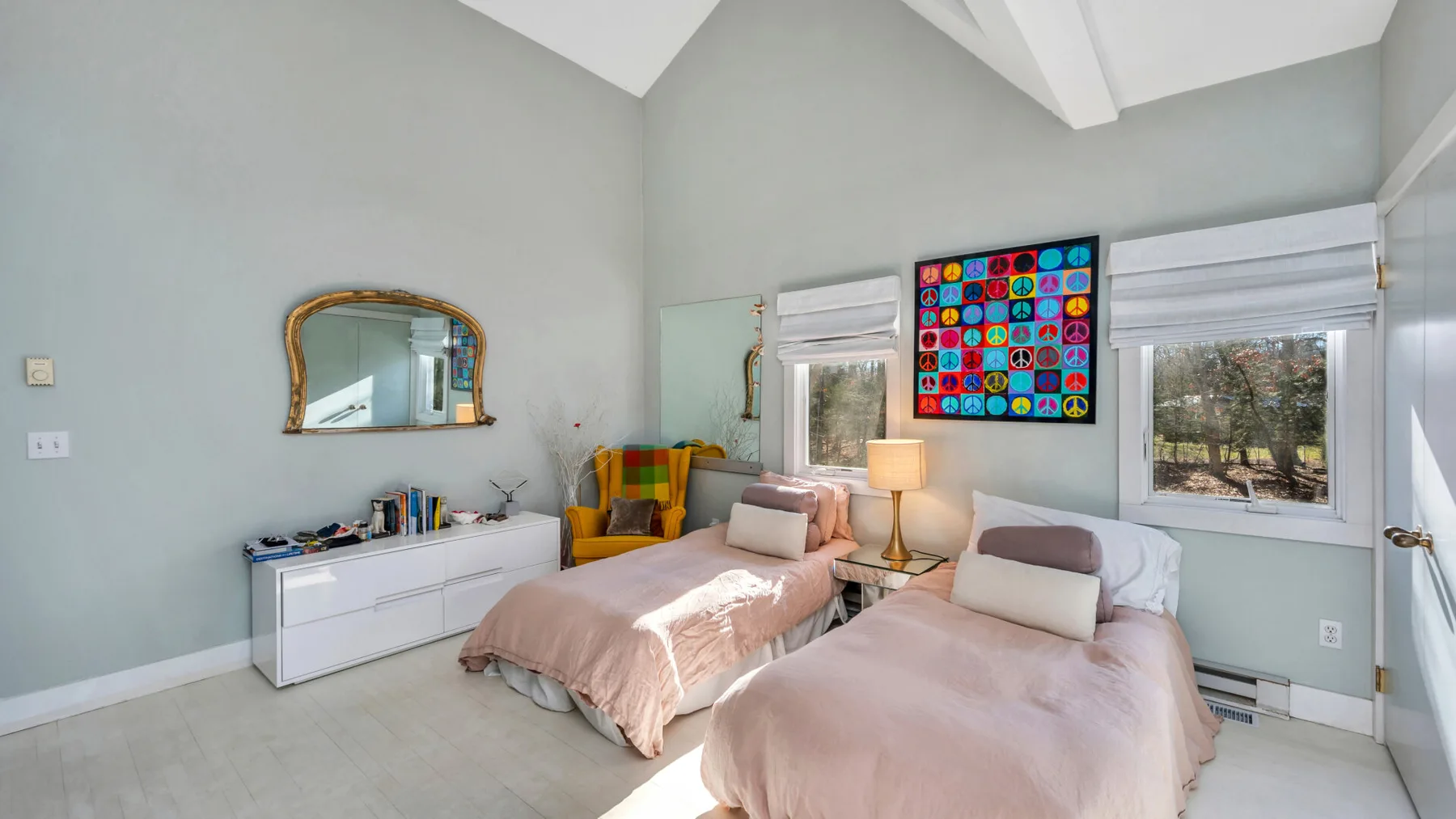 Un dormitorio luminoso con dos camas, ropa de cama clara y arte colorido en la pared.