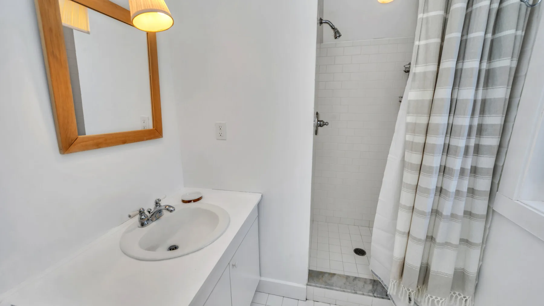 Un lavabo con espejo está junto a una ducha con azulejos.