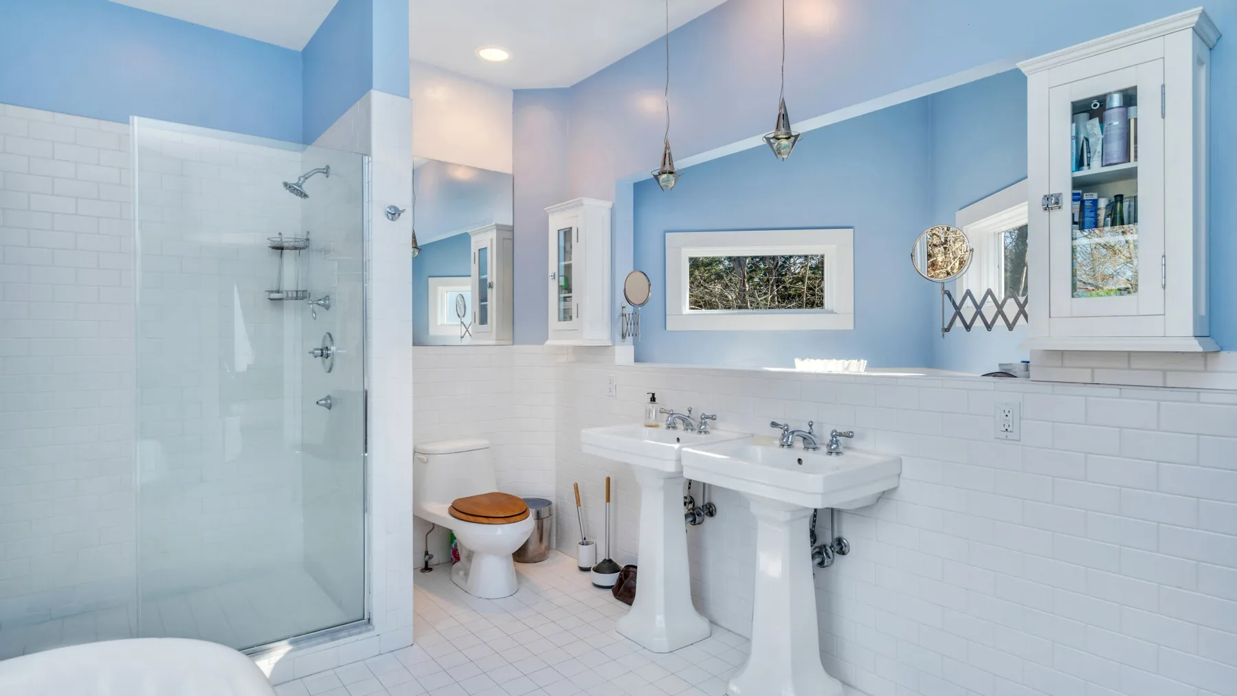 Un baño luminoso con una ducha de vidrio y lavabos de pedestal.