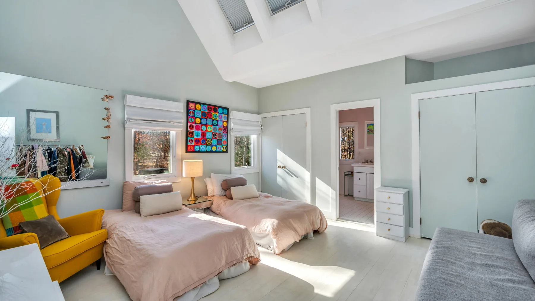 Un dormitorio luminoso con dos camas, un sillón amarillo y tragaluces.