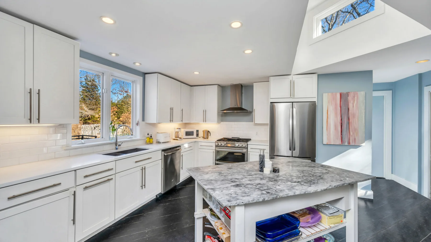 Una cocina luminosa con gabinetes blancos, electrodomésticos de acero inoxidable y una gran isla central.