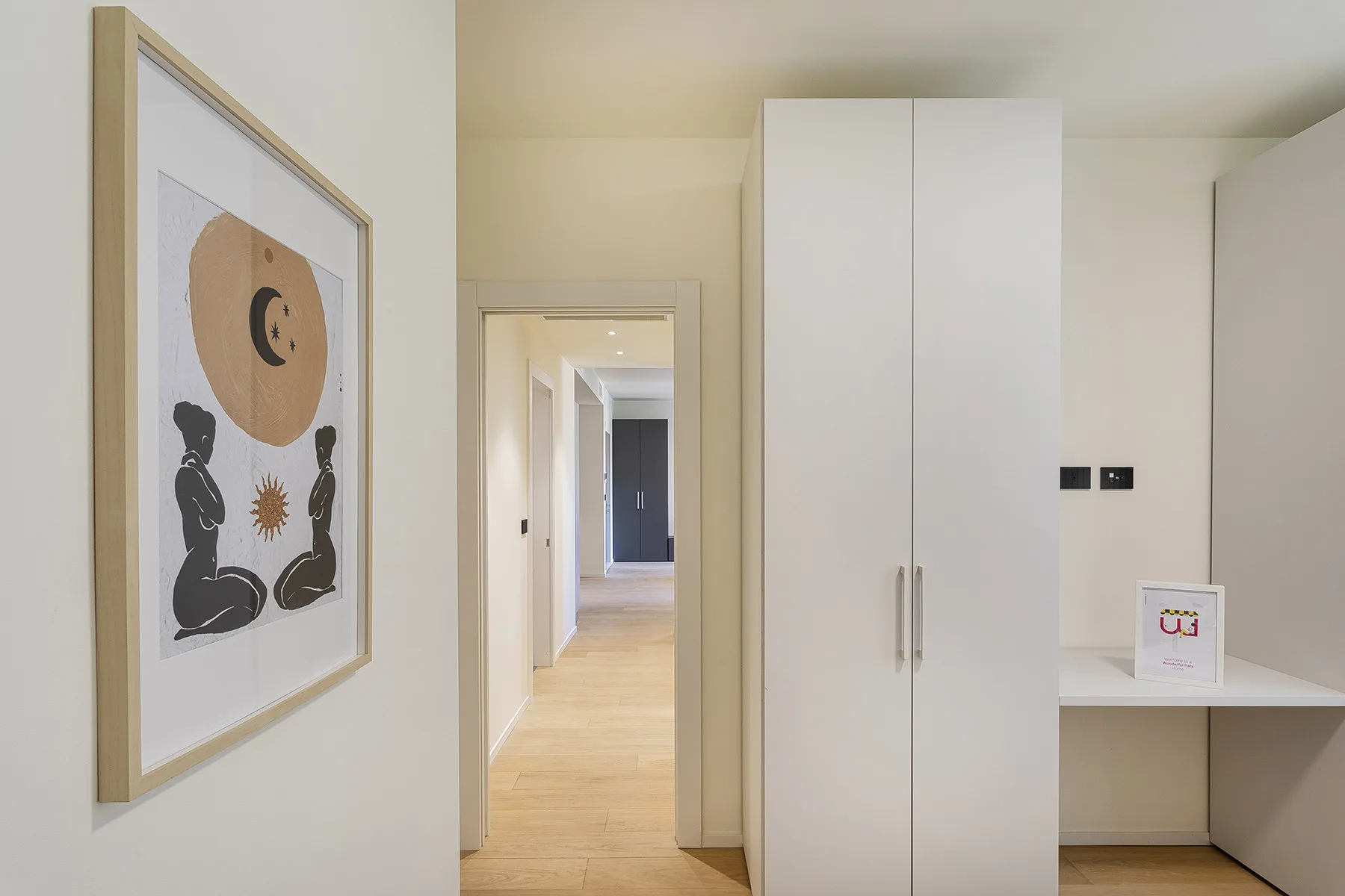 A bright interior hallway with framed artwork and a tall white storage cabinet.