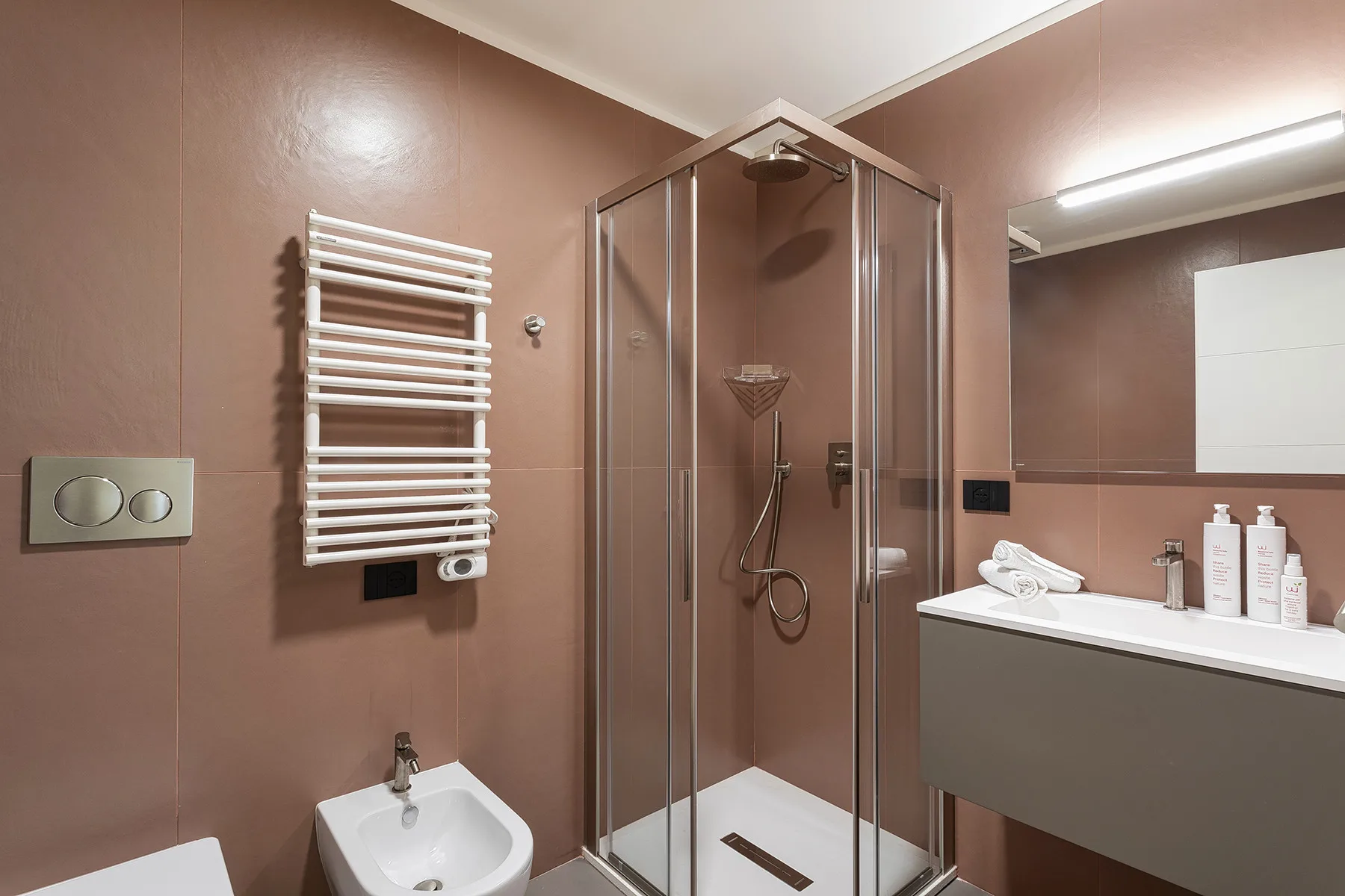 A bathroom with a glass shower, wall-mounted towel warmer, and sink.