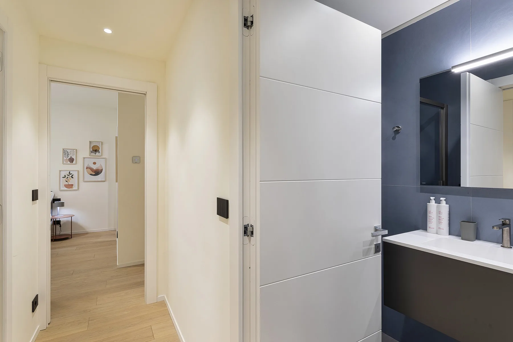 A bathroom with a white vanity and mirror opens onto a hallway.