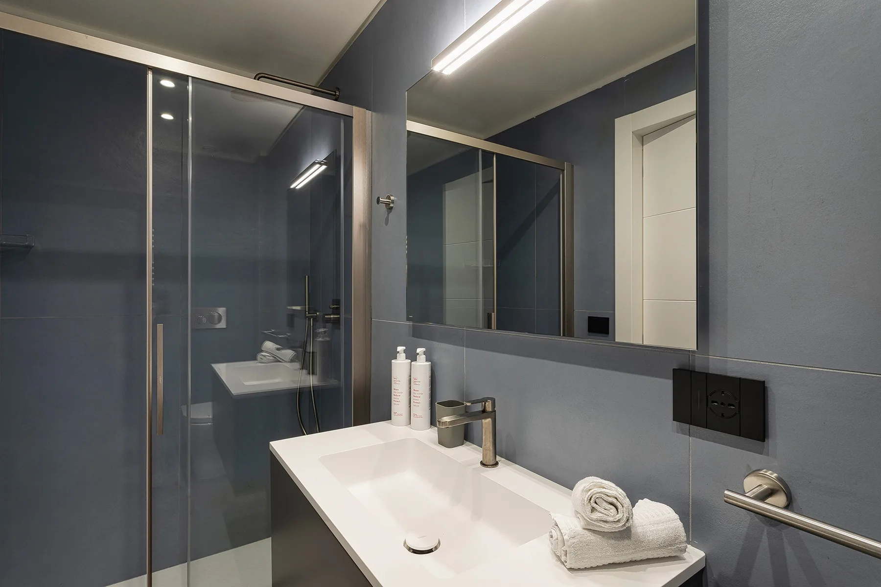 A modern bathroom with a white sink, large mirror, and glass shower.