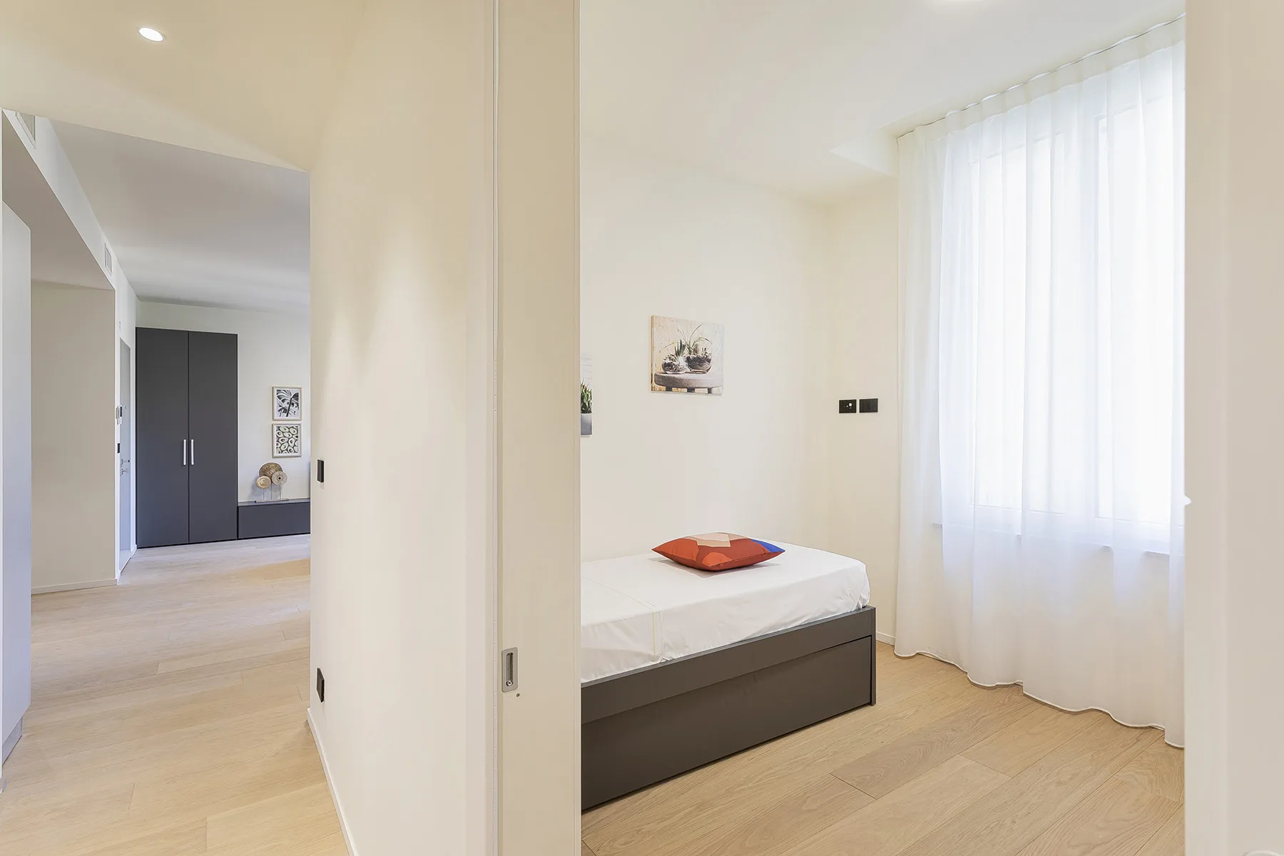 A bright bedroom with a bed beside a large curtained window.
