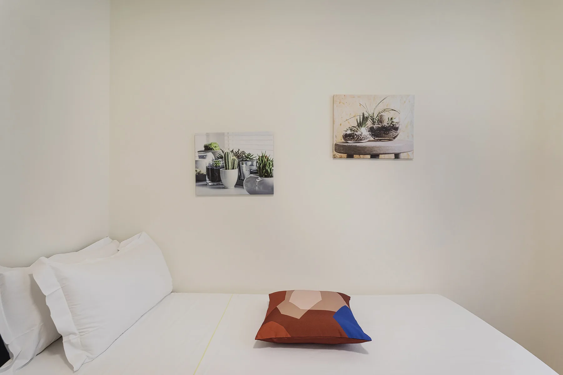 A bedroom with white bedding and two plant prints on the wall.
