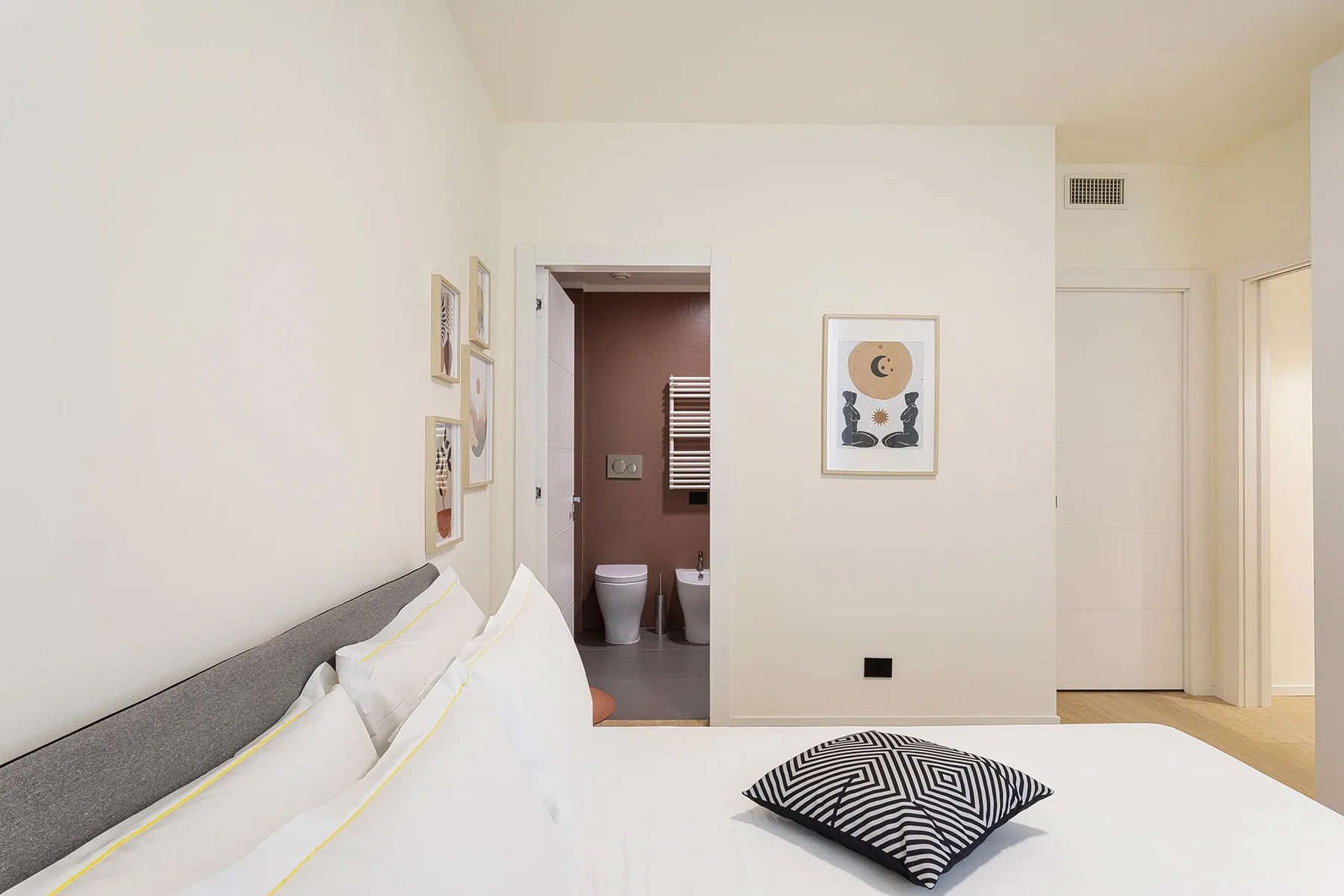 A bright bedroom with white bedding and an open doorway to a bathroom.