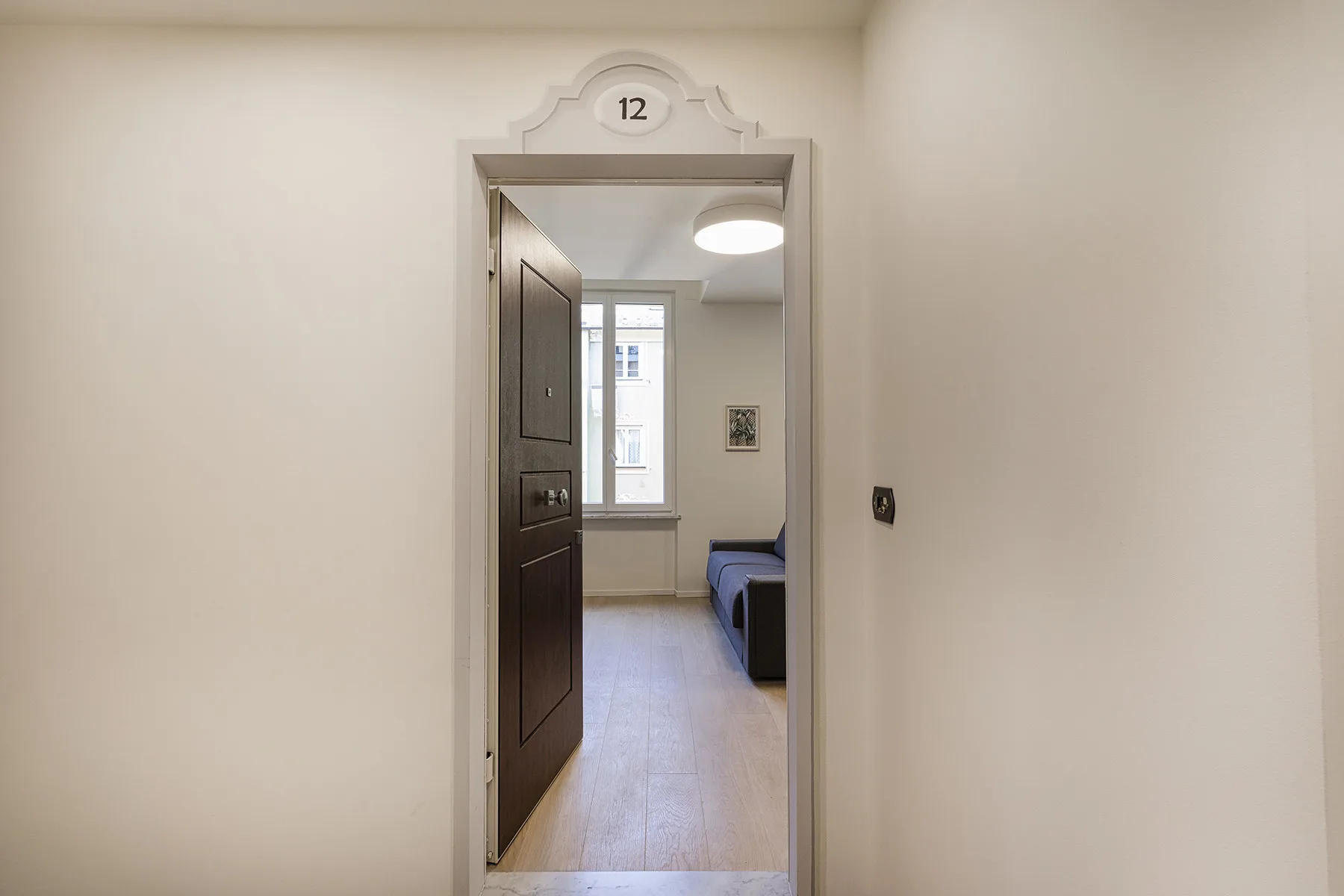 A hallway doorway opens into a room with a window and seating.
