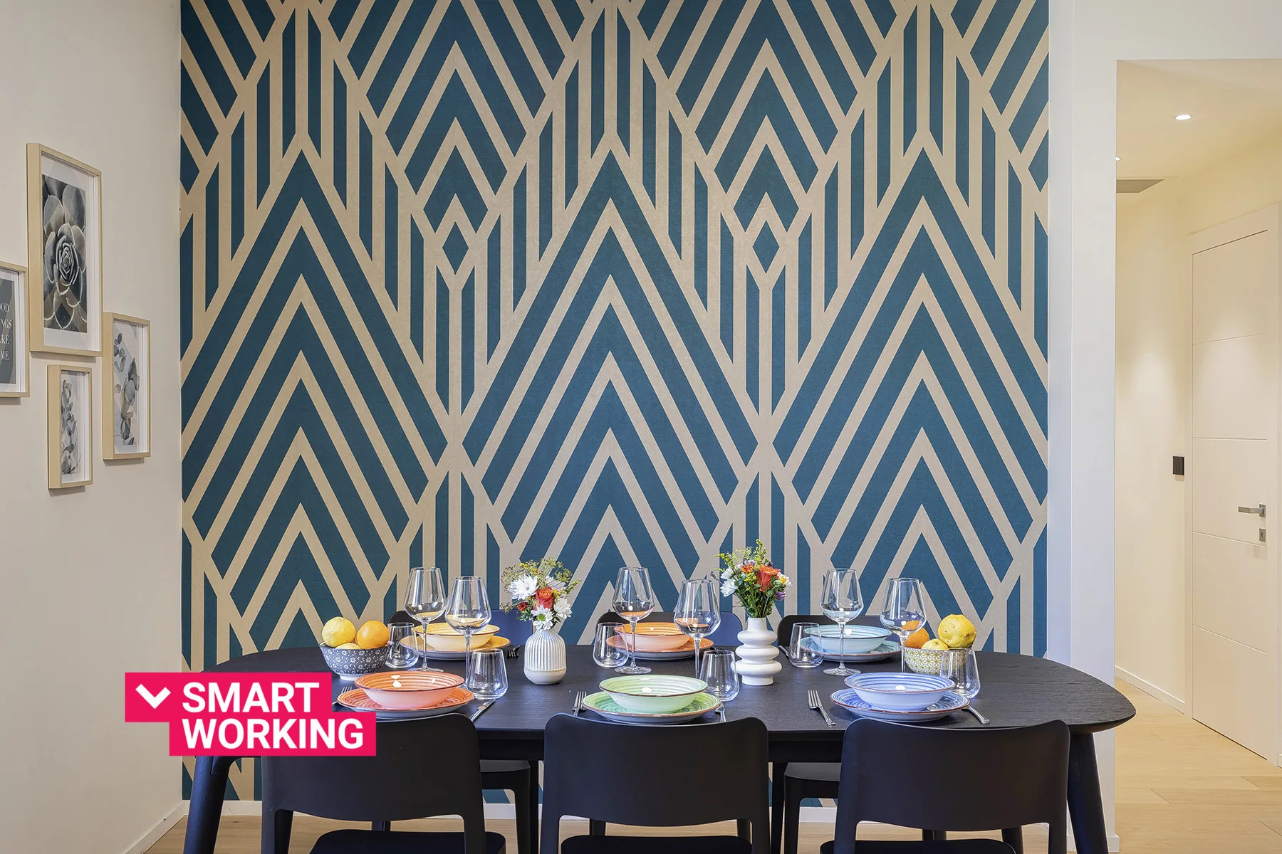 A dining table is set for a meal in front of a bold geometric accent wall.