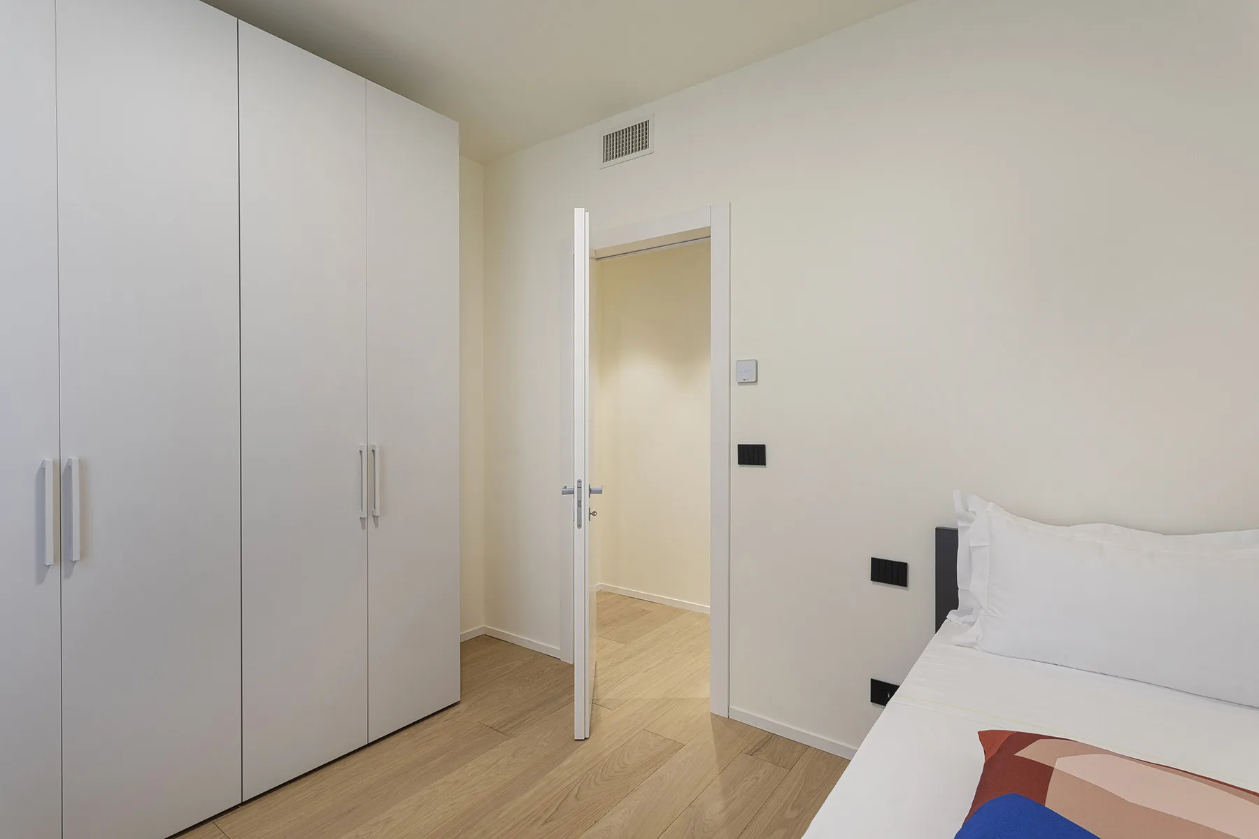 A bright bedroom with white wardrobes and a bed beside an open doorway.