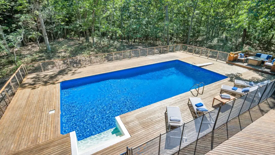 Una piscina está rodeada por una terraza de madera y árboles.