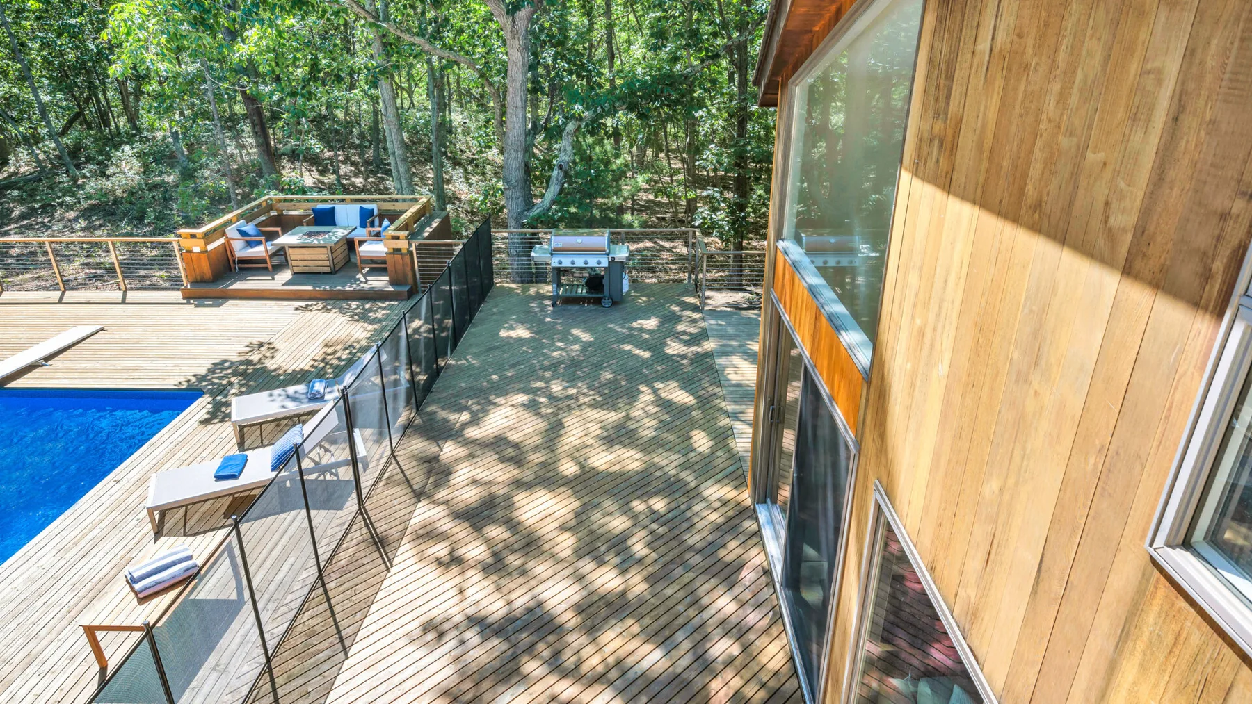 Una terraza exterior entre árboles, junto a una piscina y un edificio revestido de madera.