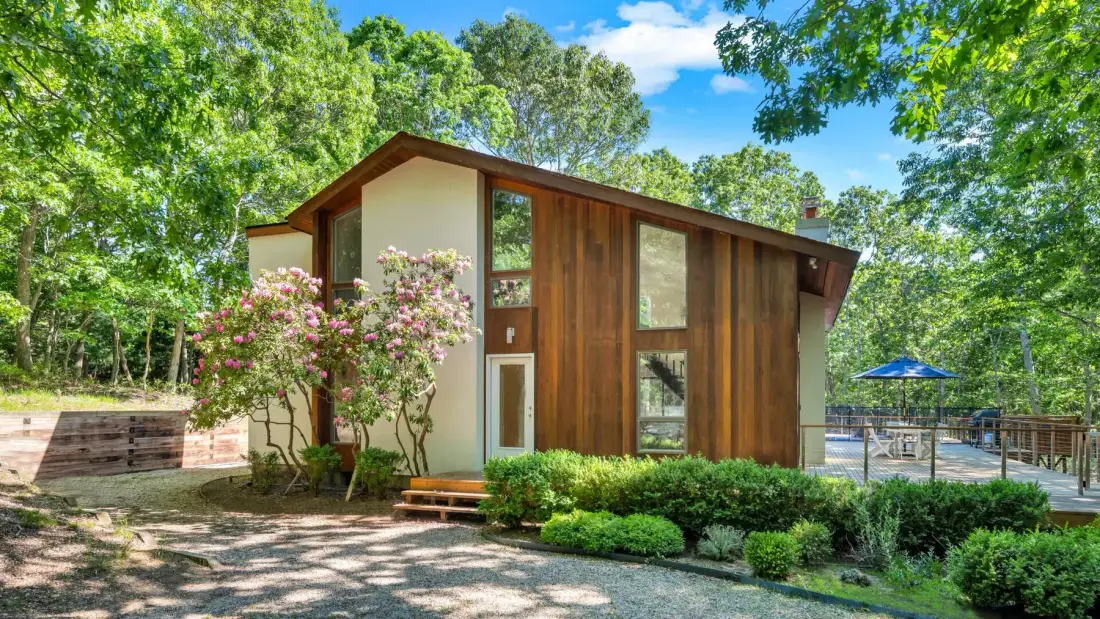 Una cabaña revestida de madera está entre árboles junto a un jardín cuidado.