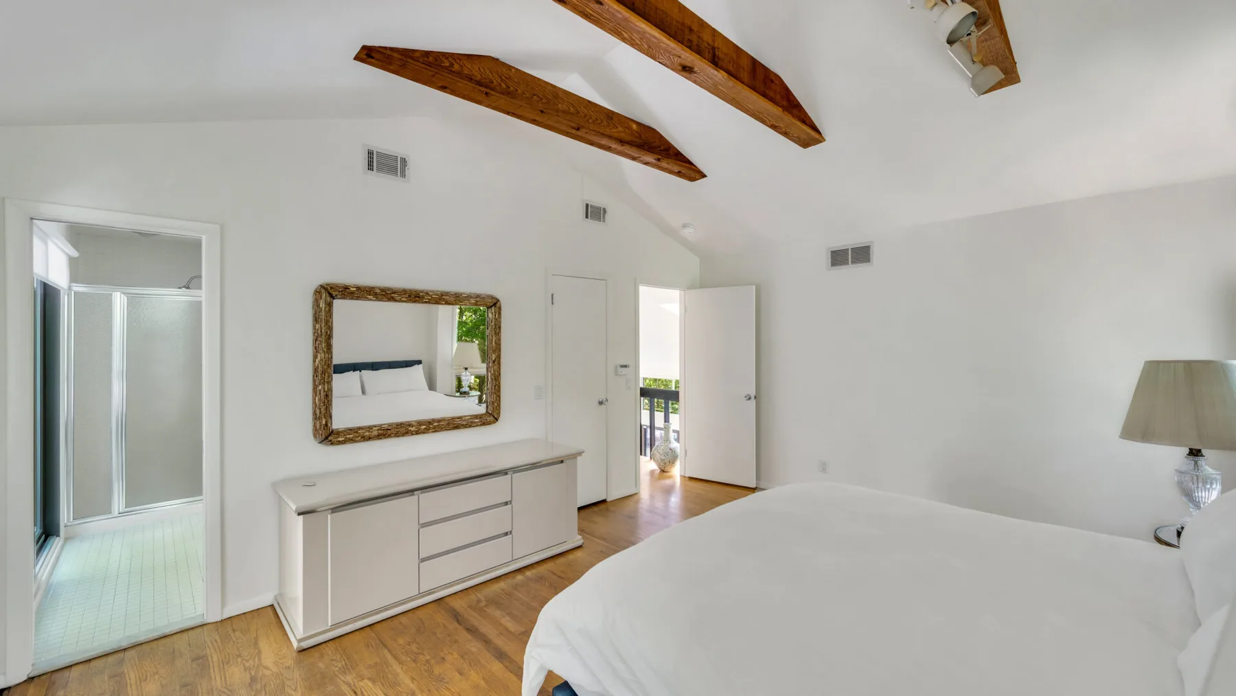 Un dormitorio luminoso con una cama grande, vigas de madera y una puerta abierta.