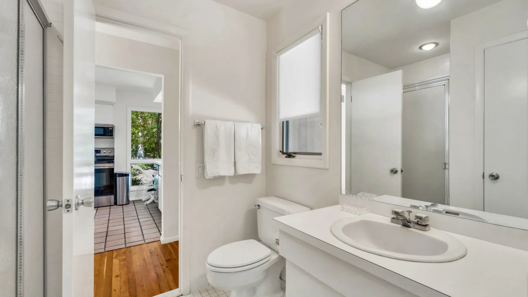 Un baño luminoso con lavabo, inodoro y un espejo grande.