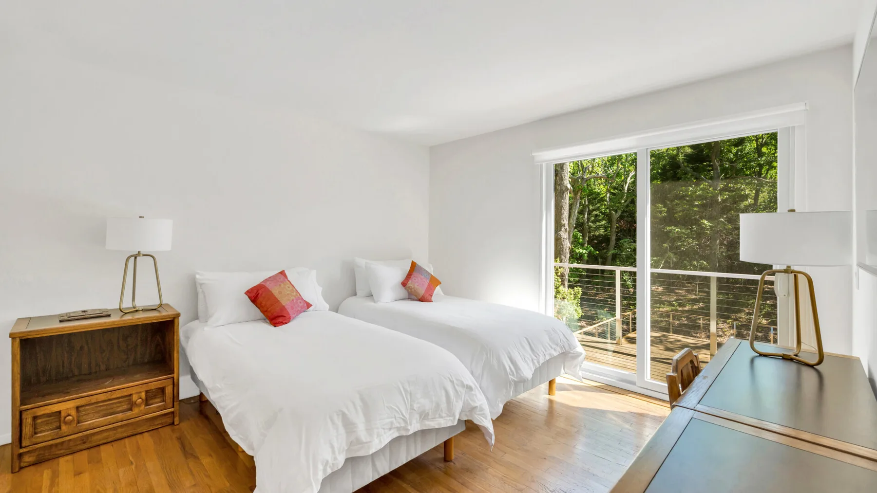 Un dormitorio luminoso con dos camas junto a una gran ventana con vistas a la vegetación.