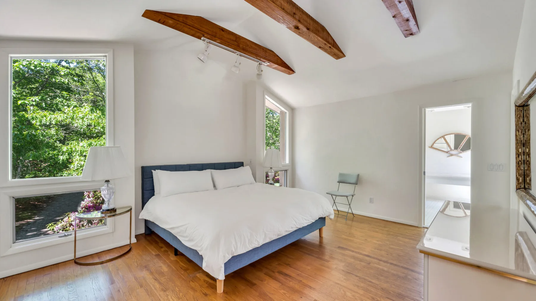 Un dormitorio luminoso con una cama, vigas de madera vistas y grandes ventanas.