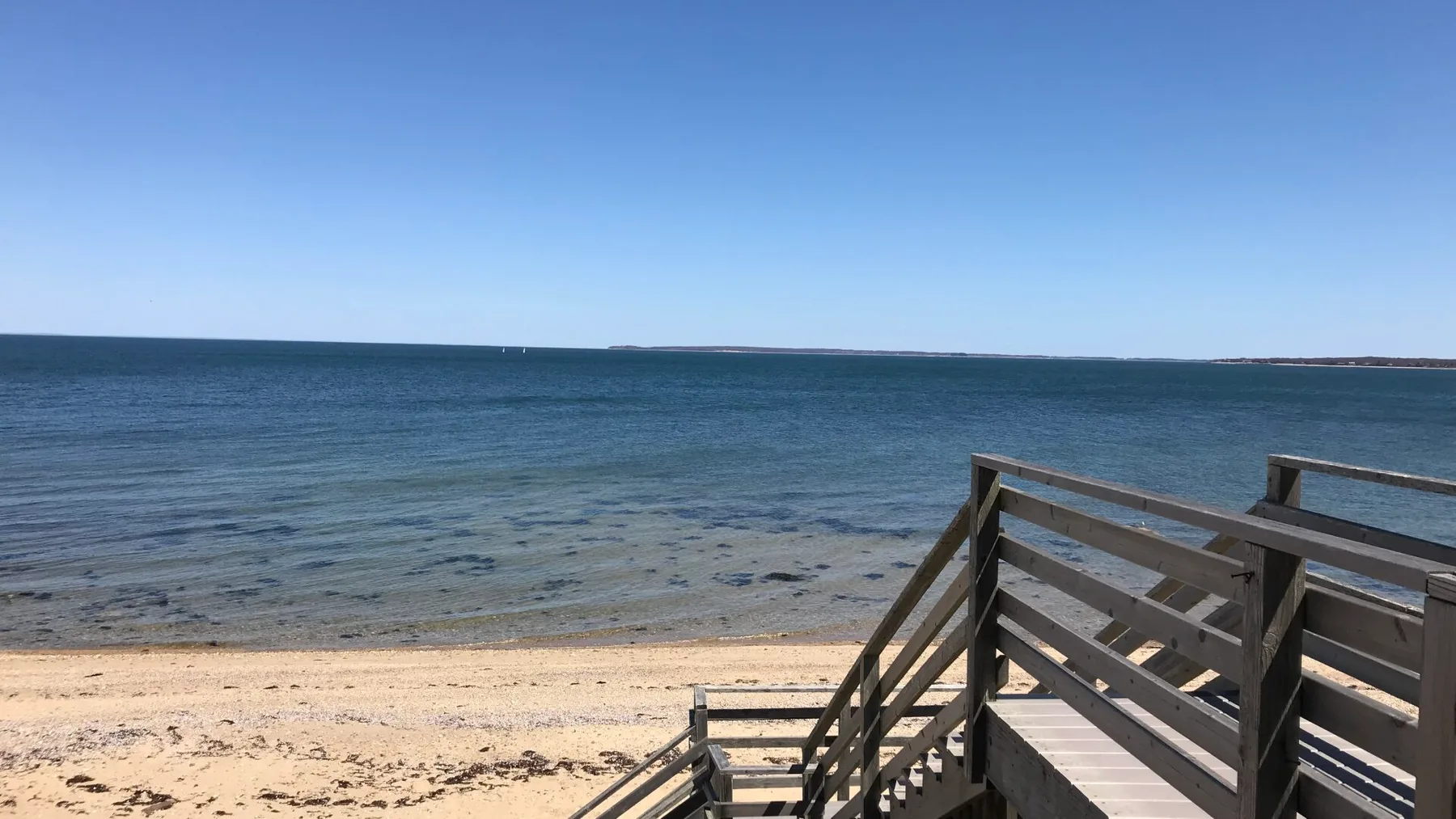Una escalera de madera baja a una playa de arena junto al agua azul tranquila.