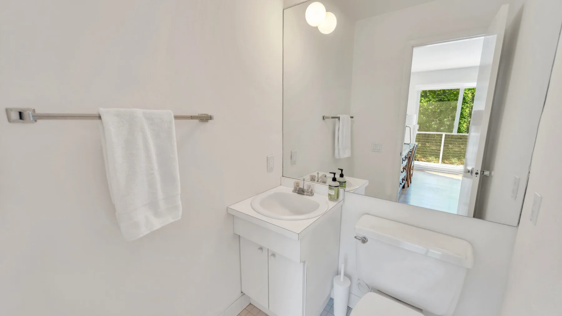 Un baño luminoso con lavabo, inodoro y un espejo grande.