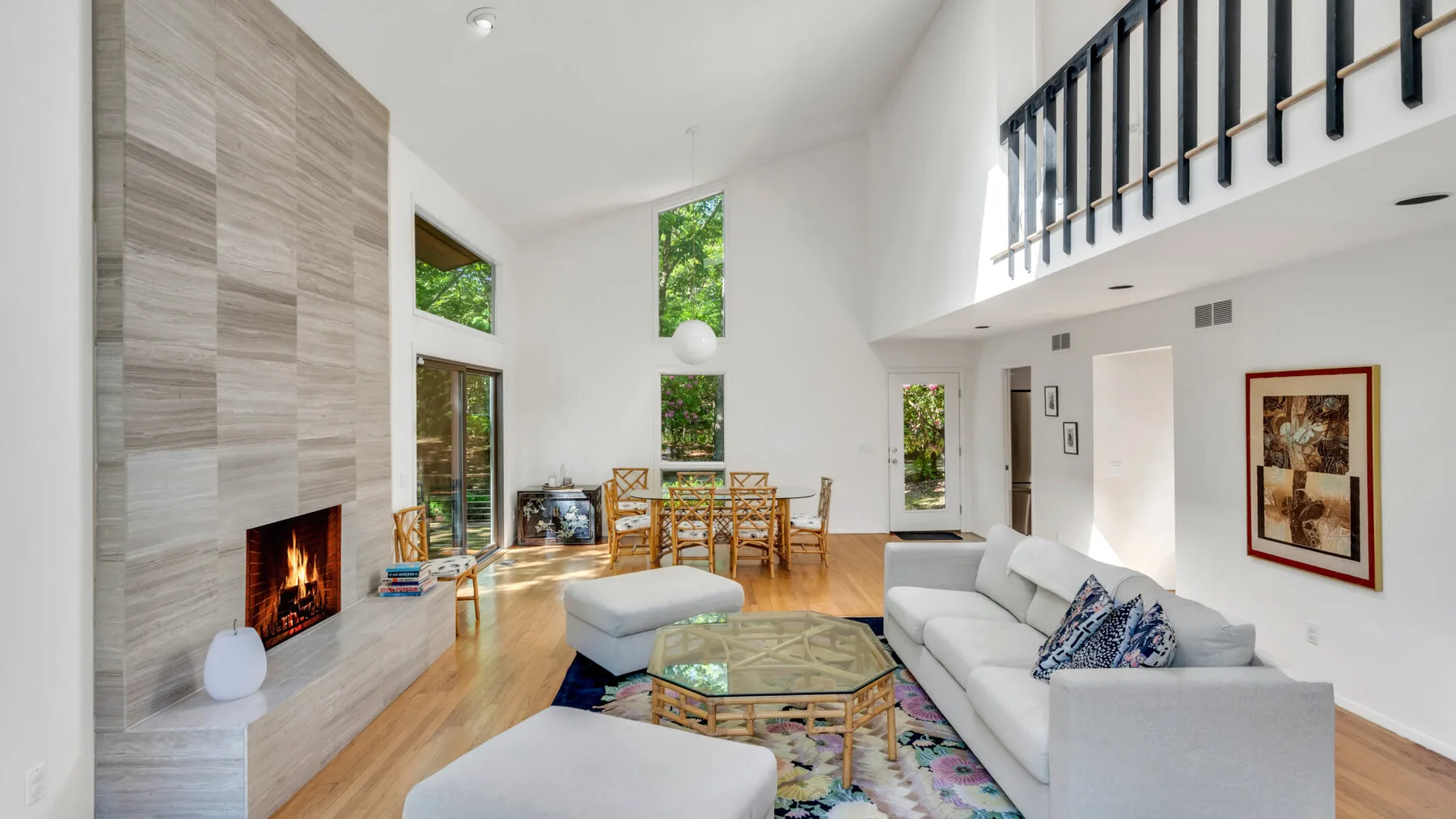 Una luminosa sala de estar de doble altura con chimenea y asientos alrededor de una mesa de centro de vidrio.