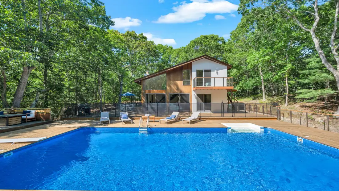 Una piscina está frente a una casa moderna rodeada de árboles.