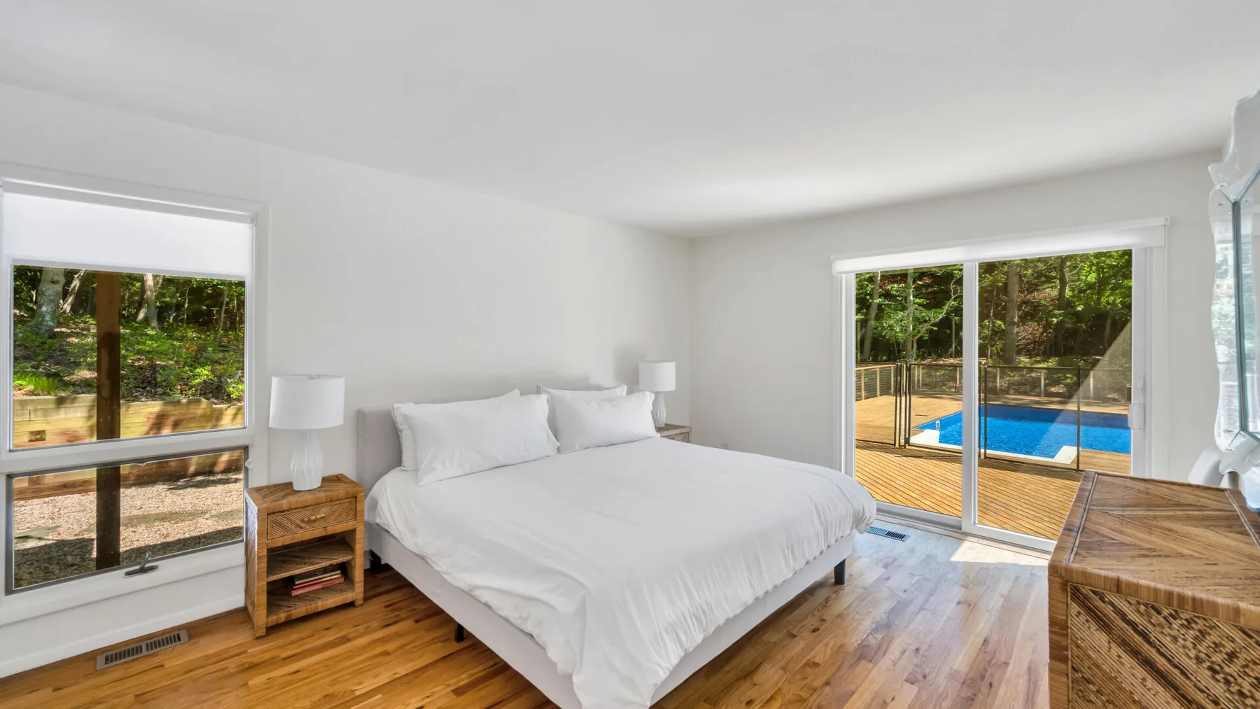 Un dormitorio luminoso con una cama blanca y puertas corredizas que dan a una piscina.