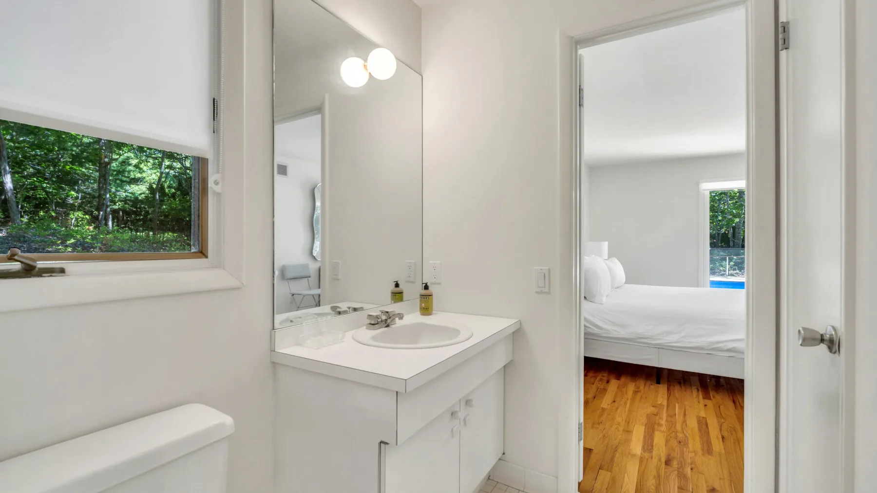 Un baño luminoso con lavabo y espejo da a un dormitorio.