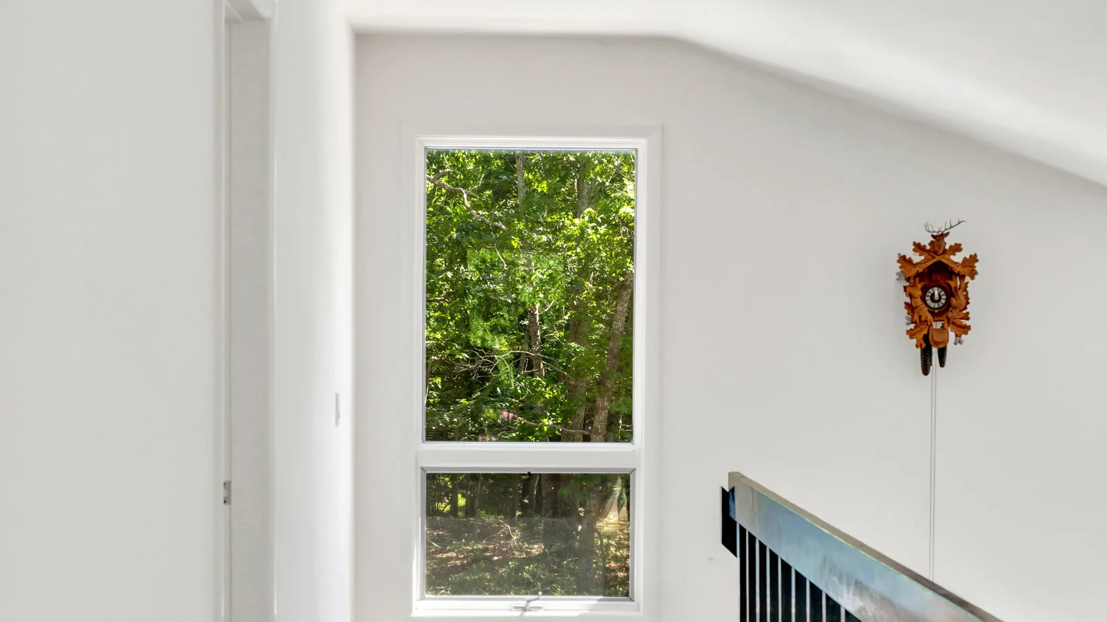 Una habitación luminosa con una ventana grande que da a árboles frondosos y un reloj de pared.