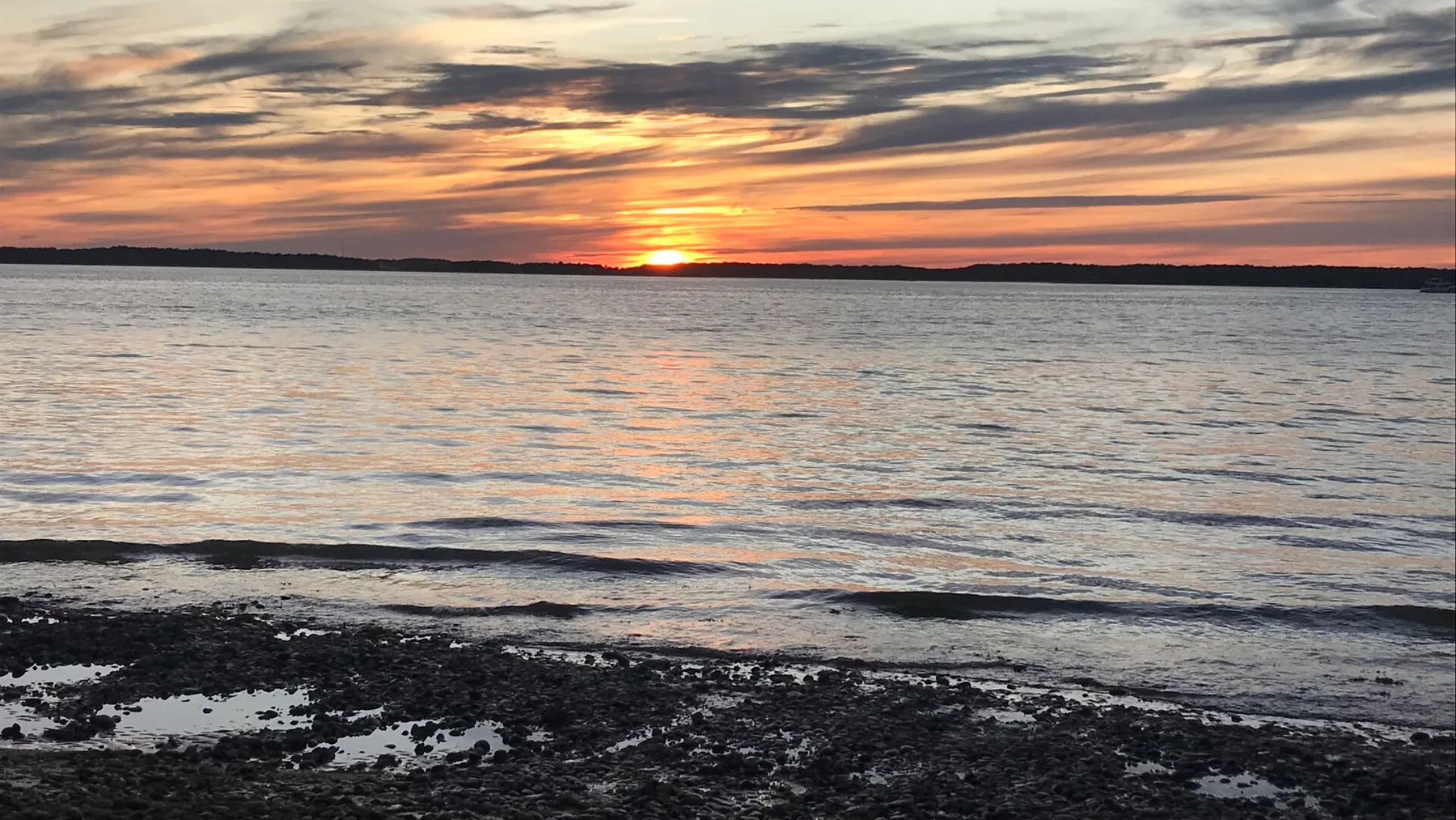 El atardecer ilumina una orilla tranquila y el agua ondulada.