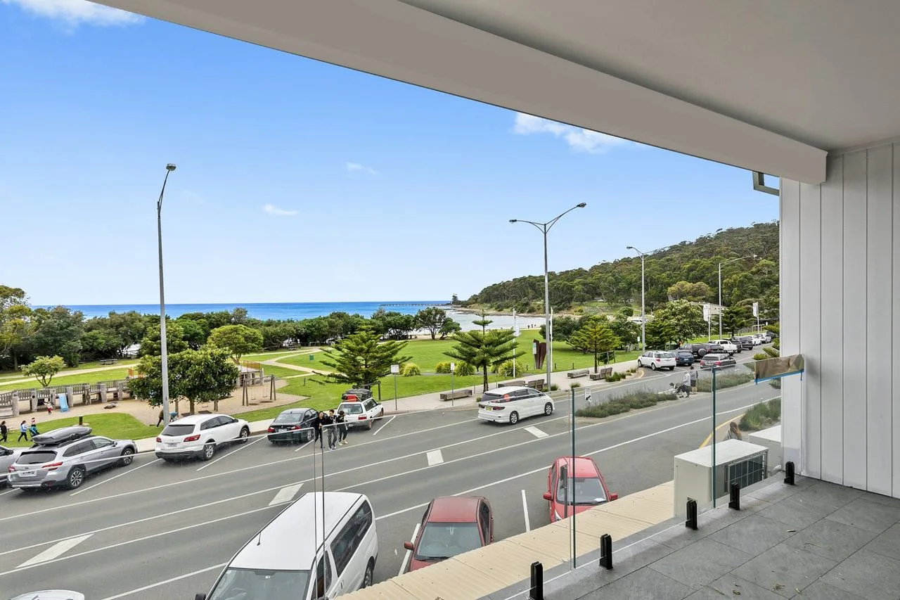 A coastal road and green park are visible from a covered balcony.