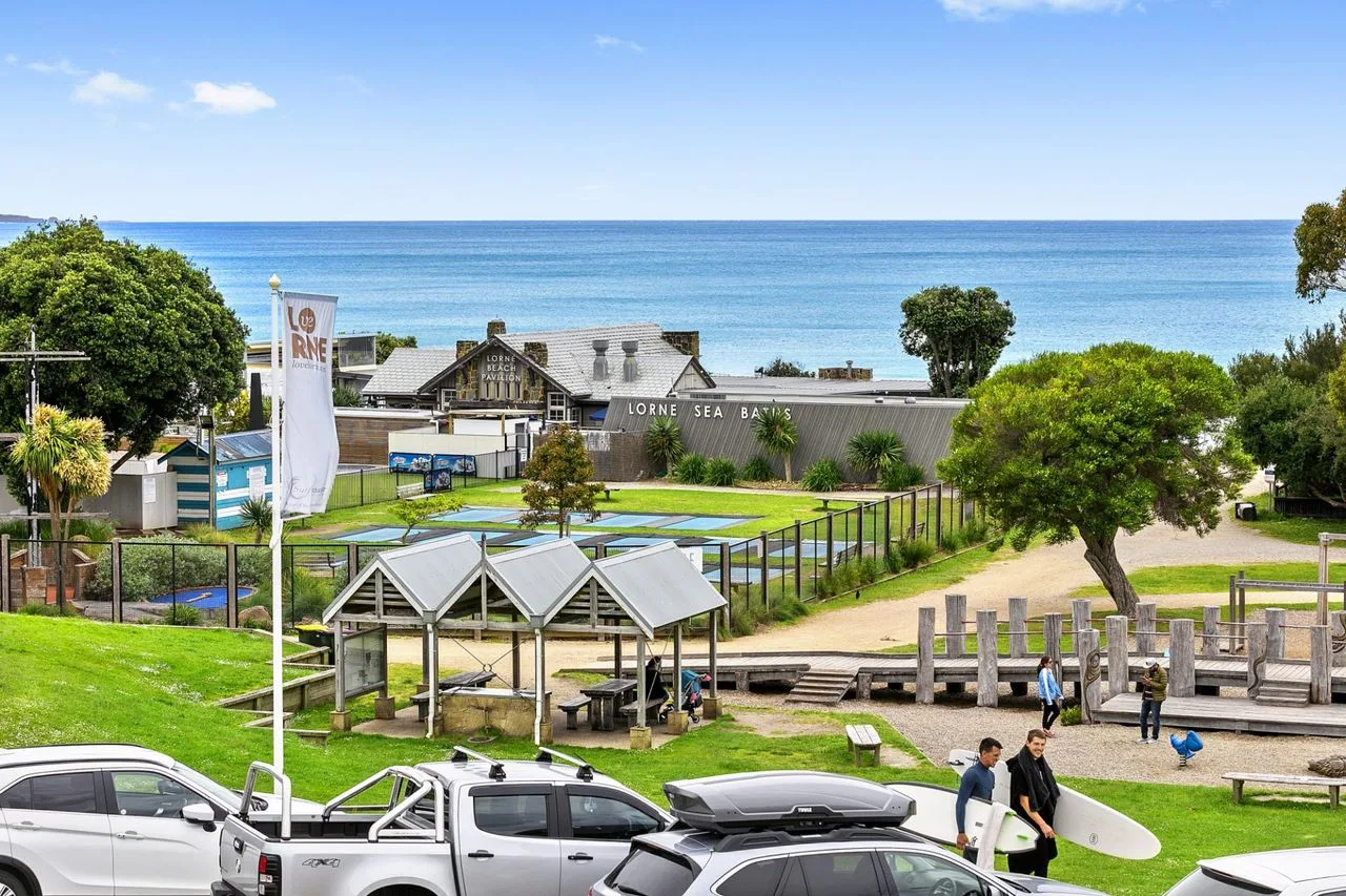 A coastal park overlooks the ocean, with a paved path and nearby buildings.
