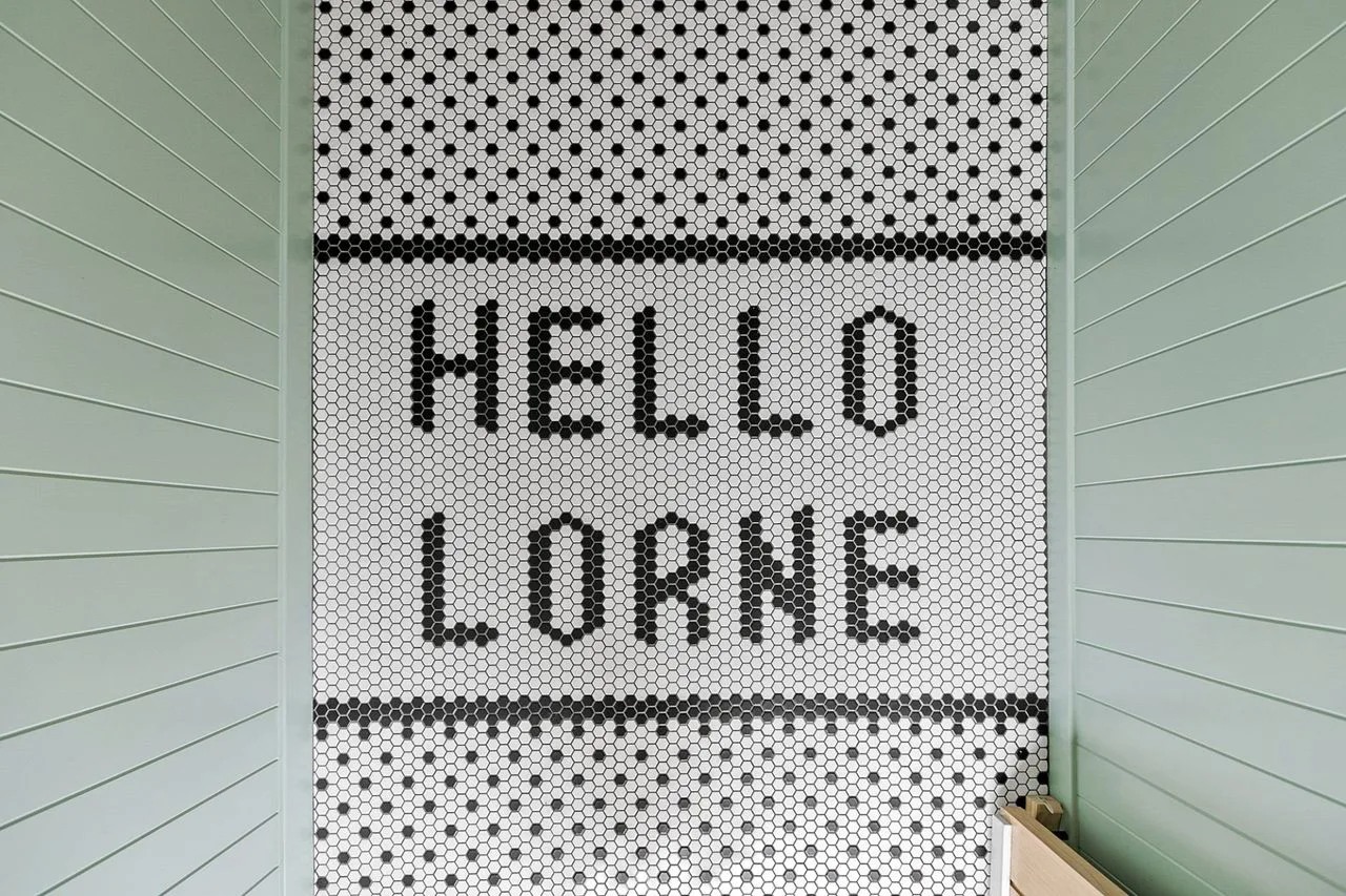 A tiled bathroom wall displays a bold black lettered message.
