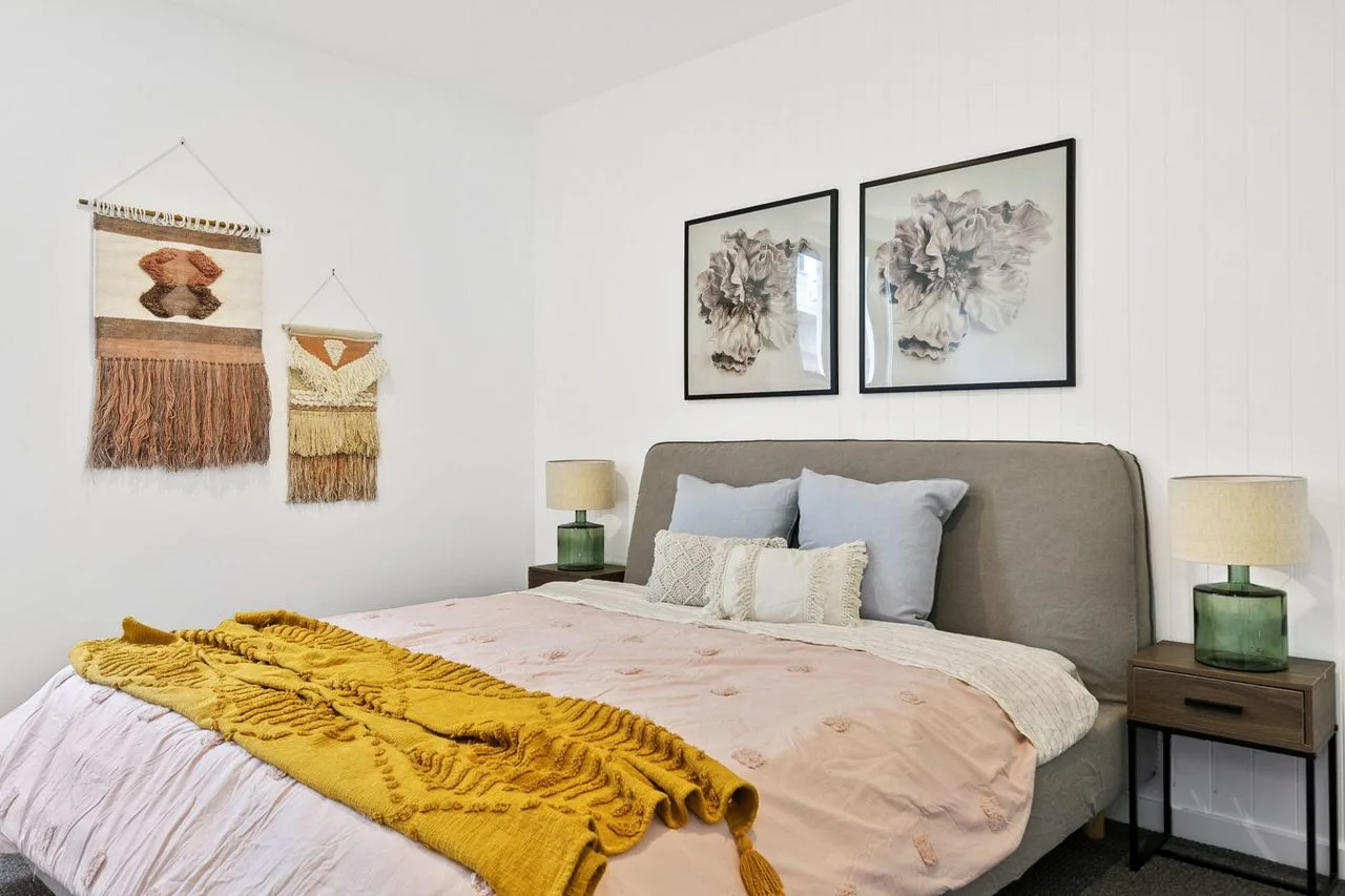 A bedroom with a neatly made bed and framed floral artwork above the headboard.