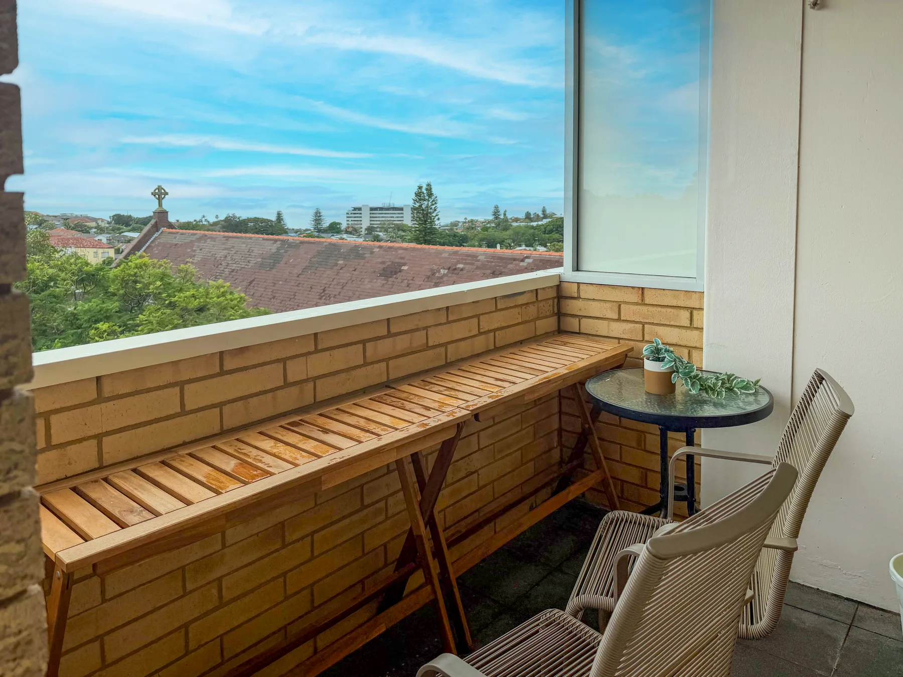 Una zona de estar en un balcón con un banco largo de madera y una mesa redonda pequeña.