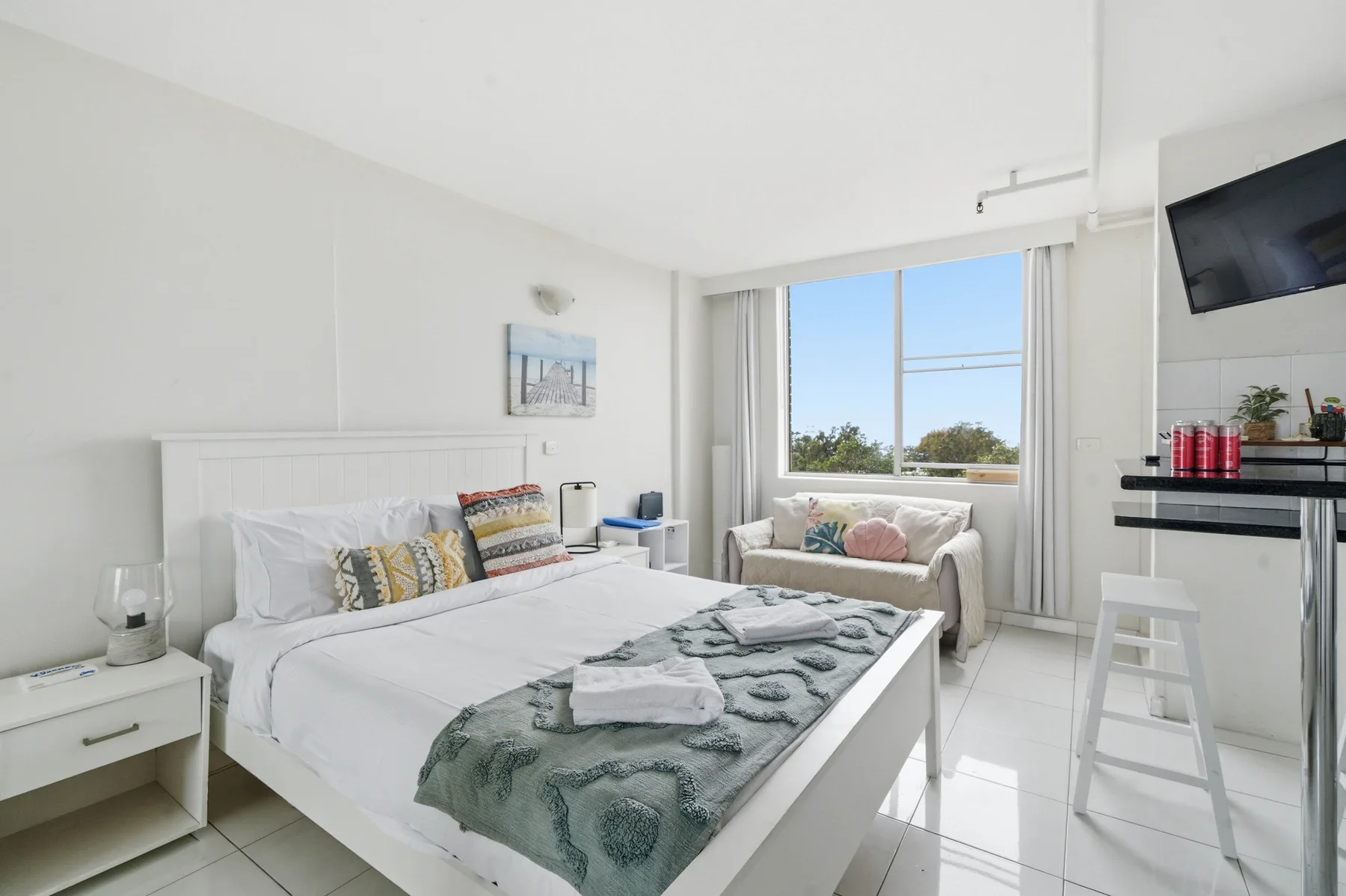 Un dormitorio luminoso con una cama bien hecha junto a una ventana grande.